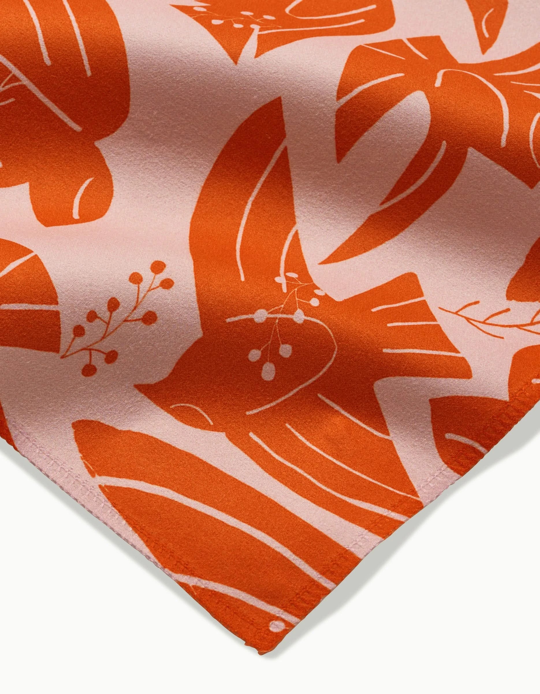Close-up of Ash Cascade’s Peace Bird dinner napkin, showcasing soft, absorbent fabric with an orange and pink bird and botanical pattern of stylized birds and berry branches.