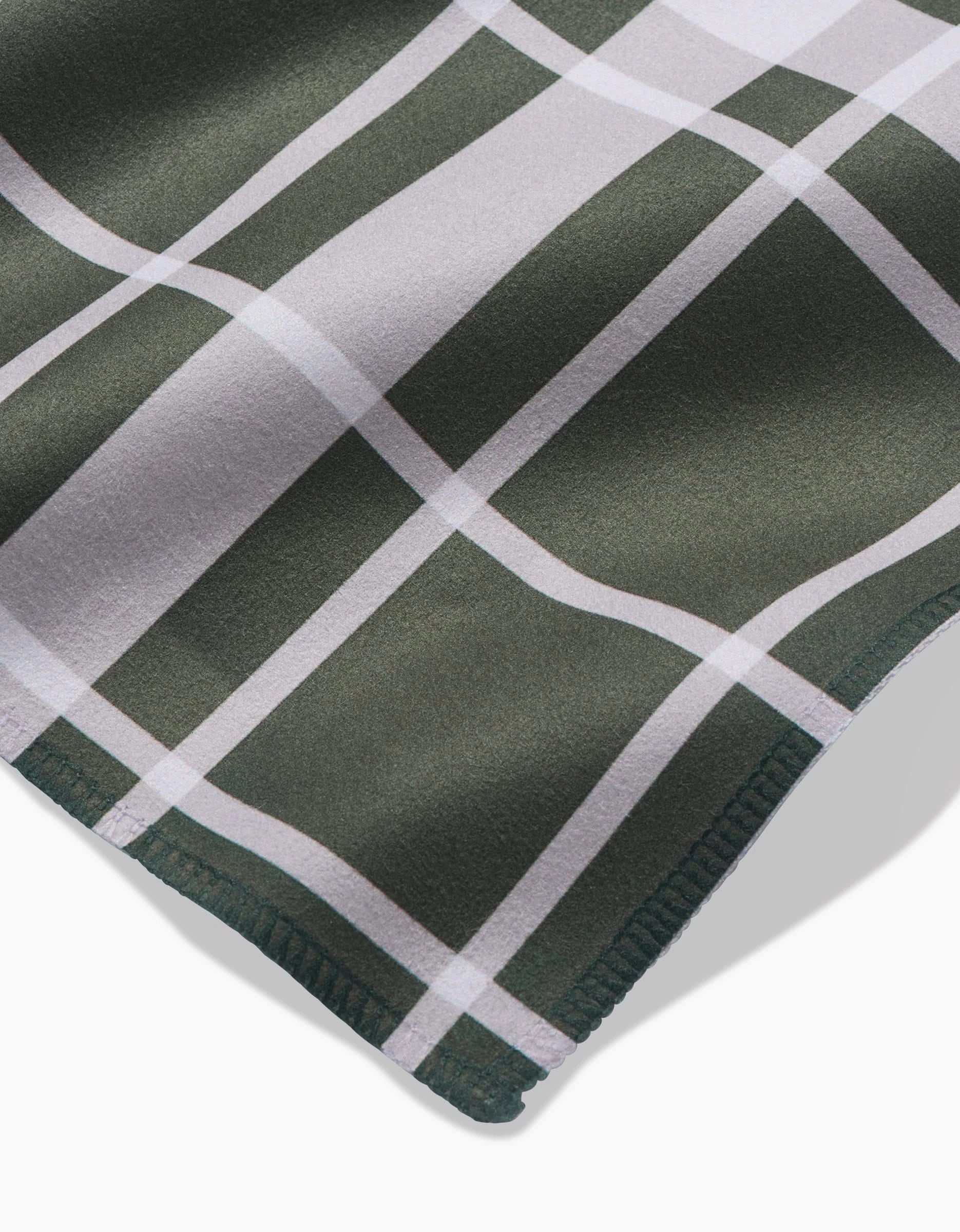A close-up of Aubrey Fairchilds Picnic Time Green napkin set features a green and white plaid pattern with intersecting stripes and finely stitched edges in soft Geosuede fabric.