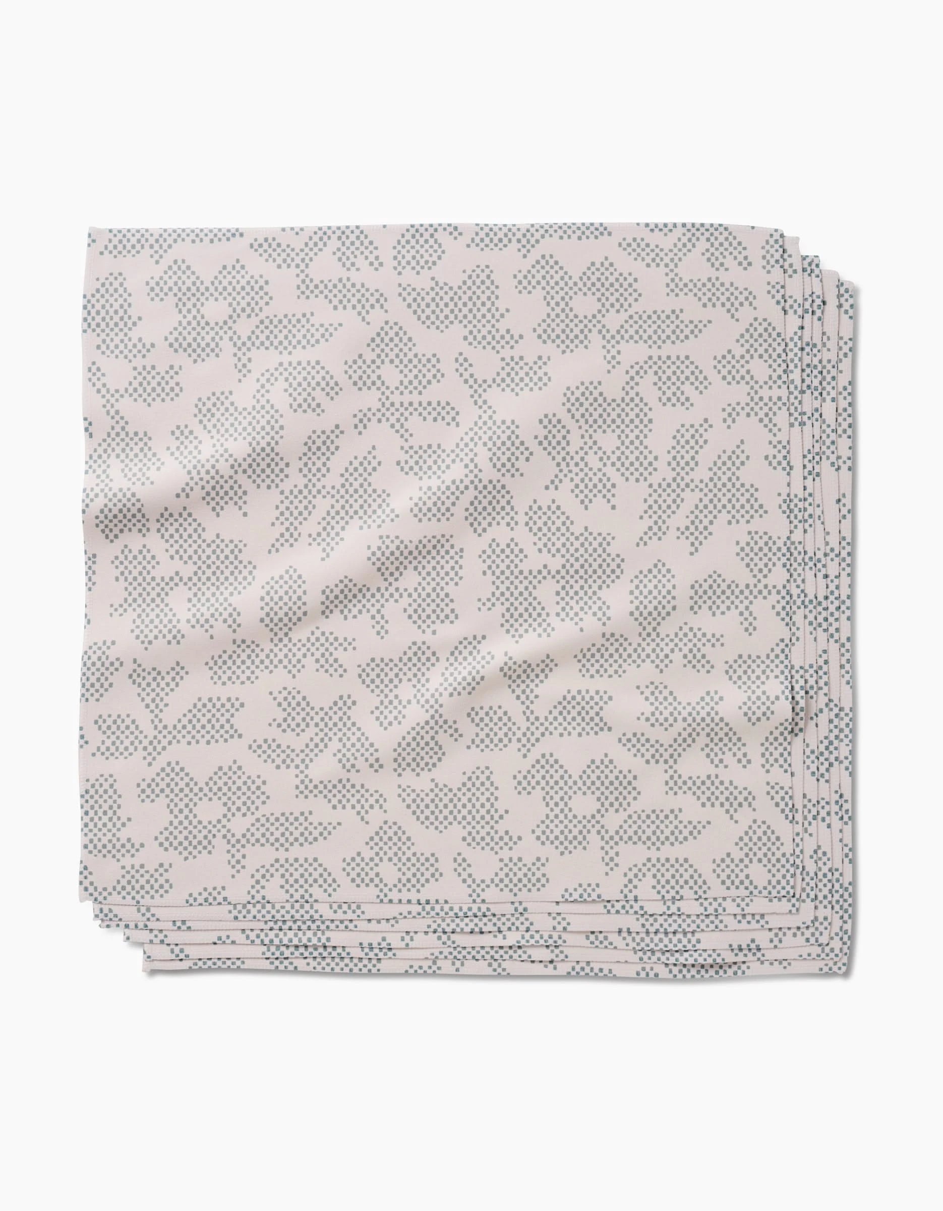 The Pixie Sage Dinner Napkin Set by Studio Jeannot features folded, light-hued Geosuede fabric with a subtle blue dotted floral pattern, elegantly displayed on a white background.