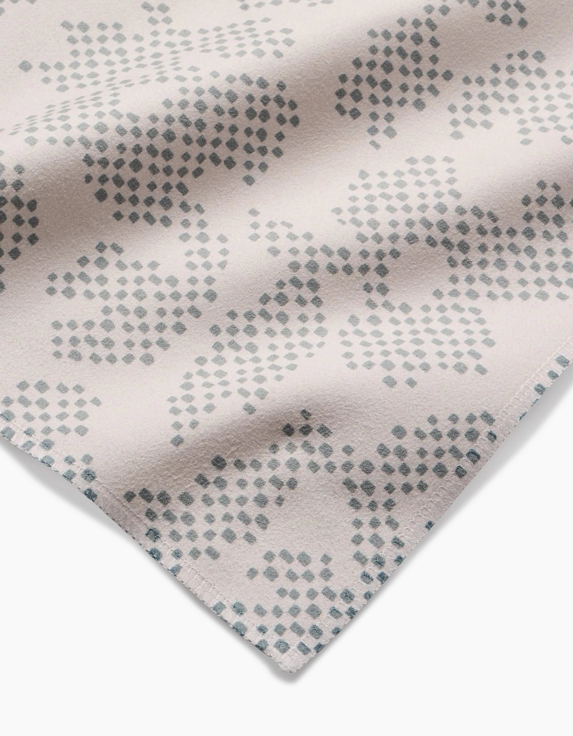 A close-up of Pixie Sage by Studio Jeannot shows beige Geosuede fabric with an abstract pattern of small gray-blue dots. Made from recycled materials, the slightly folded corner highlights its geometric design.