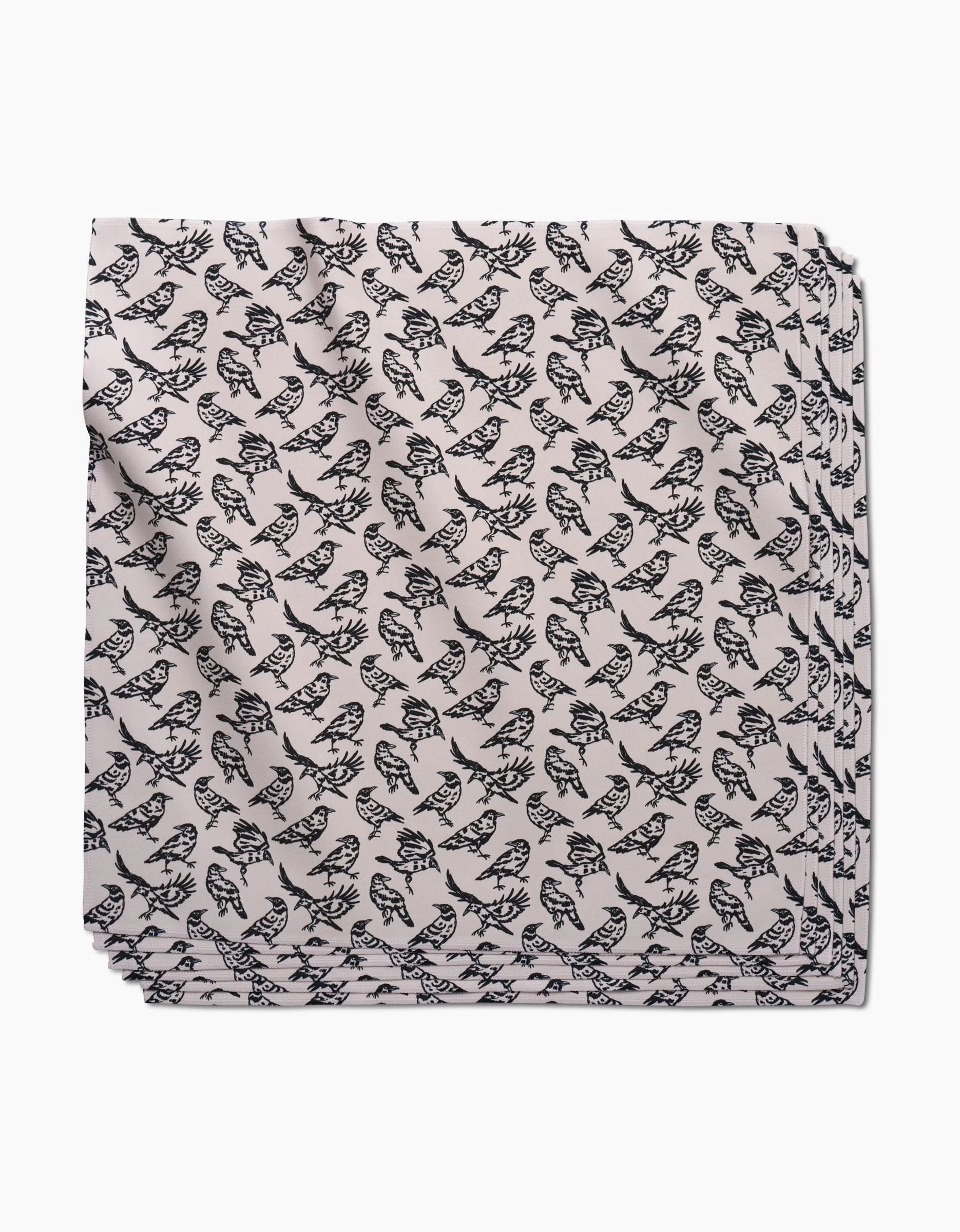 The Kayla Ann Raven napkin is a neatly folded, light-colored recycled dinner napkin featuring a repeating black fish pattern, shown on a white background.