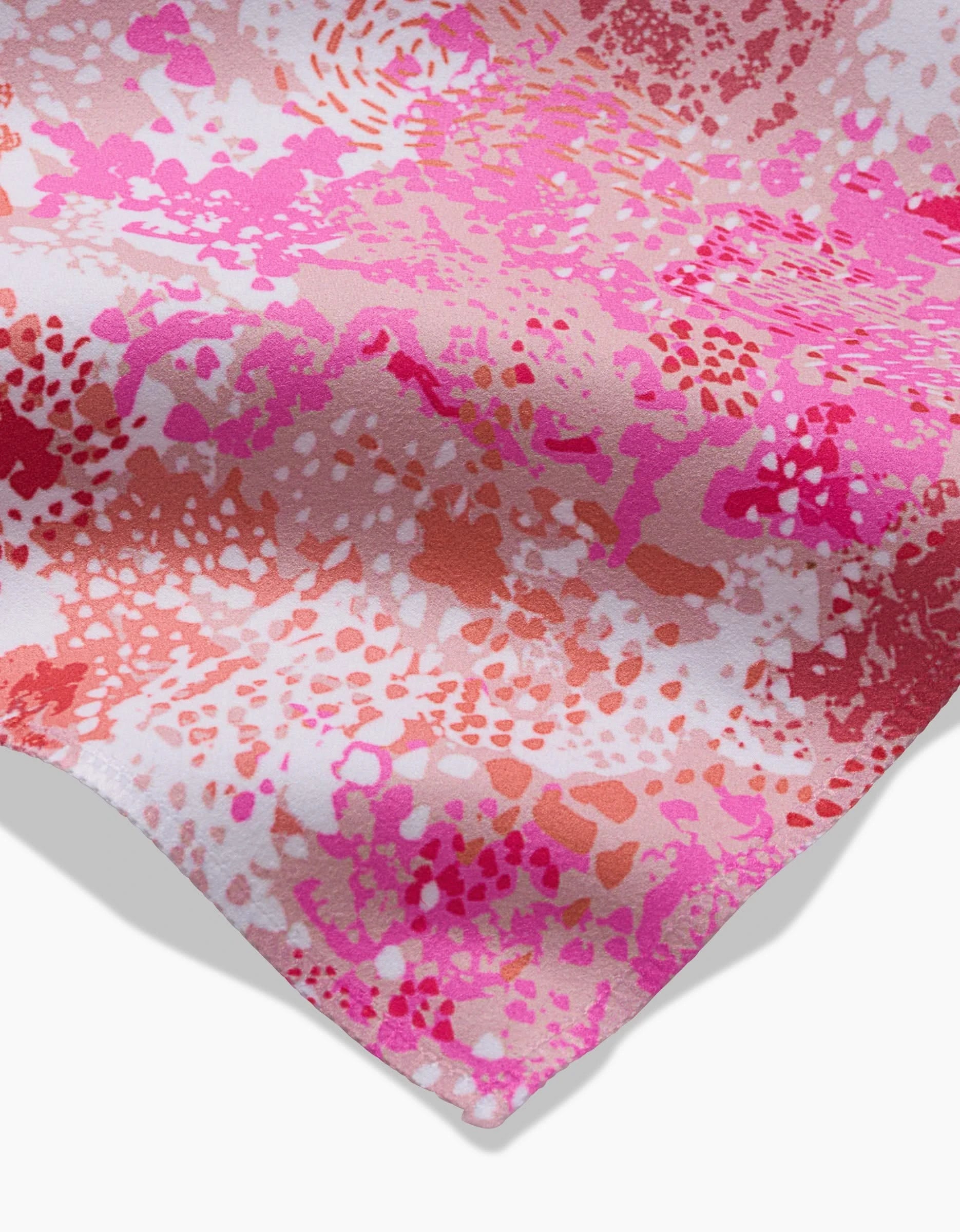 A close-up of the Rawhide dinner napkin by Elisabeth Wing, featuring Geosuede fabric with a vibrant abstract pattern in pink, red, and white, adorned with scattered irregular spots and splashes.