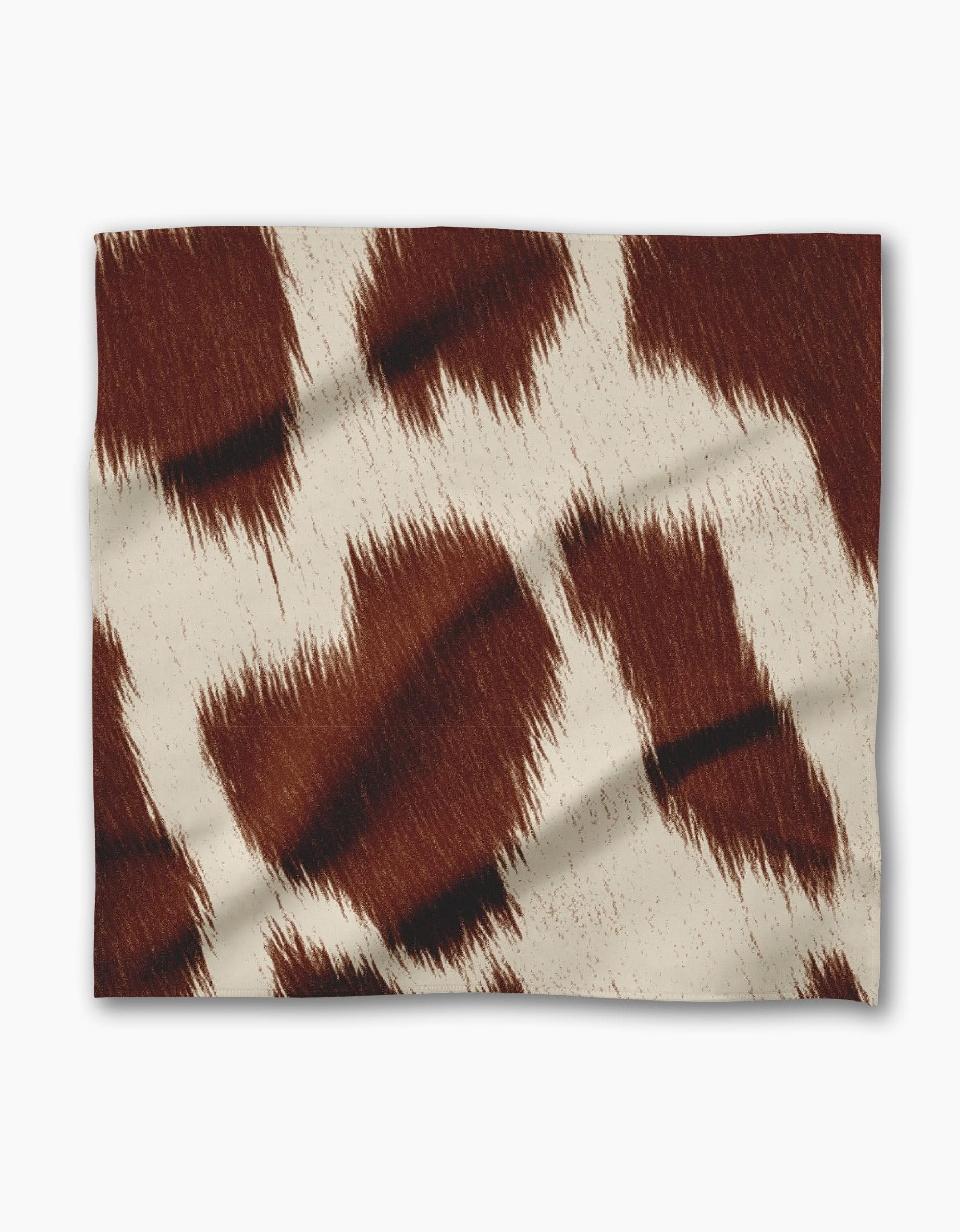 The Geometry Rodeo blanket features a brown and white cowhide pattern with jagged patches and subtle texture, pairing perfectly with eco-friendly or reusable dinner napkins for rustic, sustainable style.