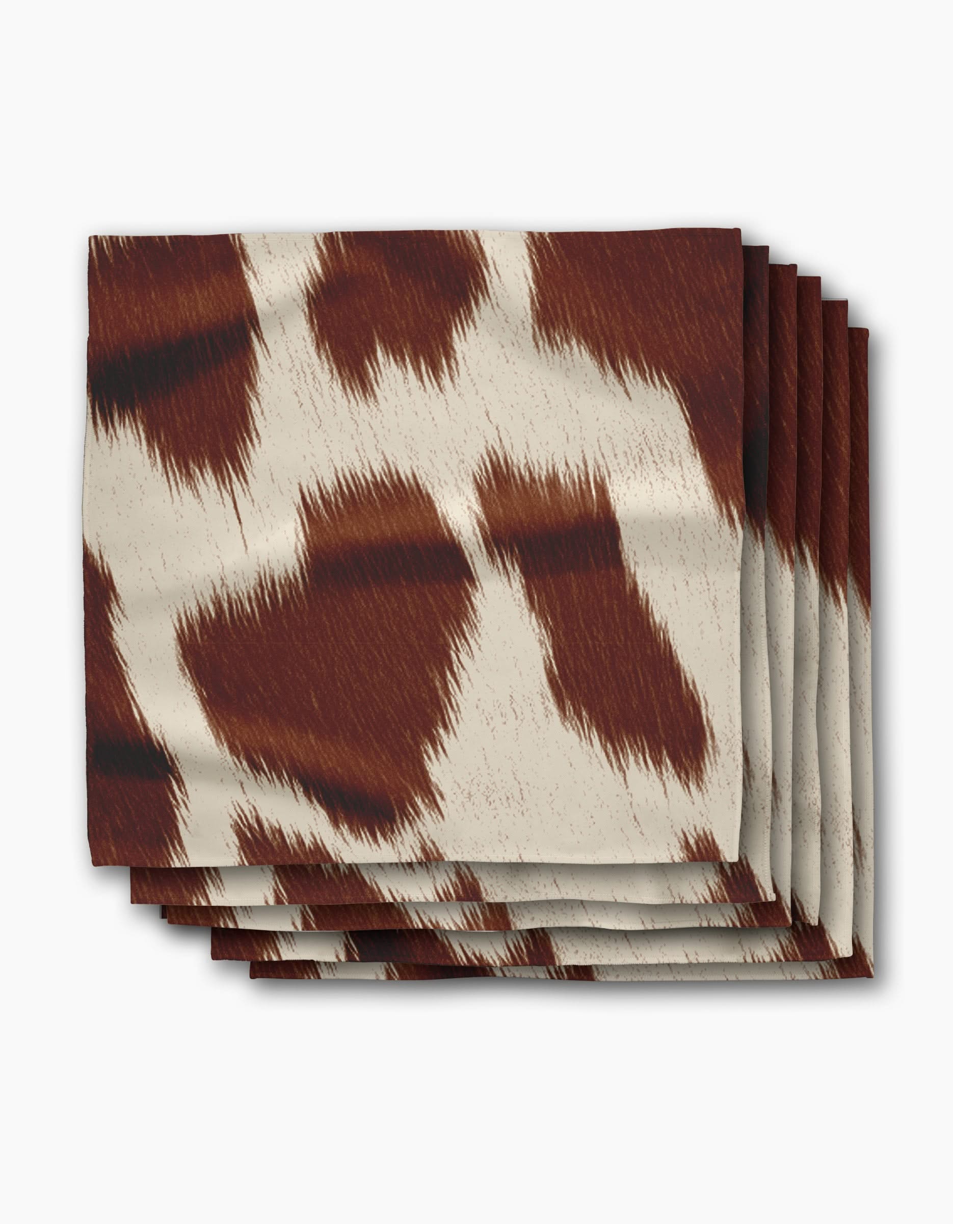 A stack of Geometry Rodeo eco-friendly napkins featuring a brown and white cowhide pattern is displayed on a plain white background.