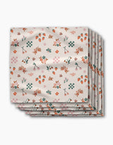 A stack of four Russet Meadow dinner napkins by Charlie Rowan Designs, made from soft Geosuede fabric, featuring a colorful pattern of flowers, leaves, strawberries, cherries, and geometric shapes on a white background.