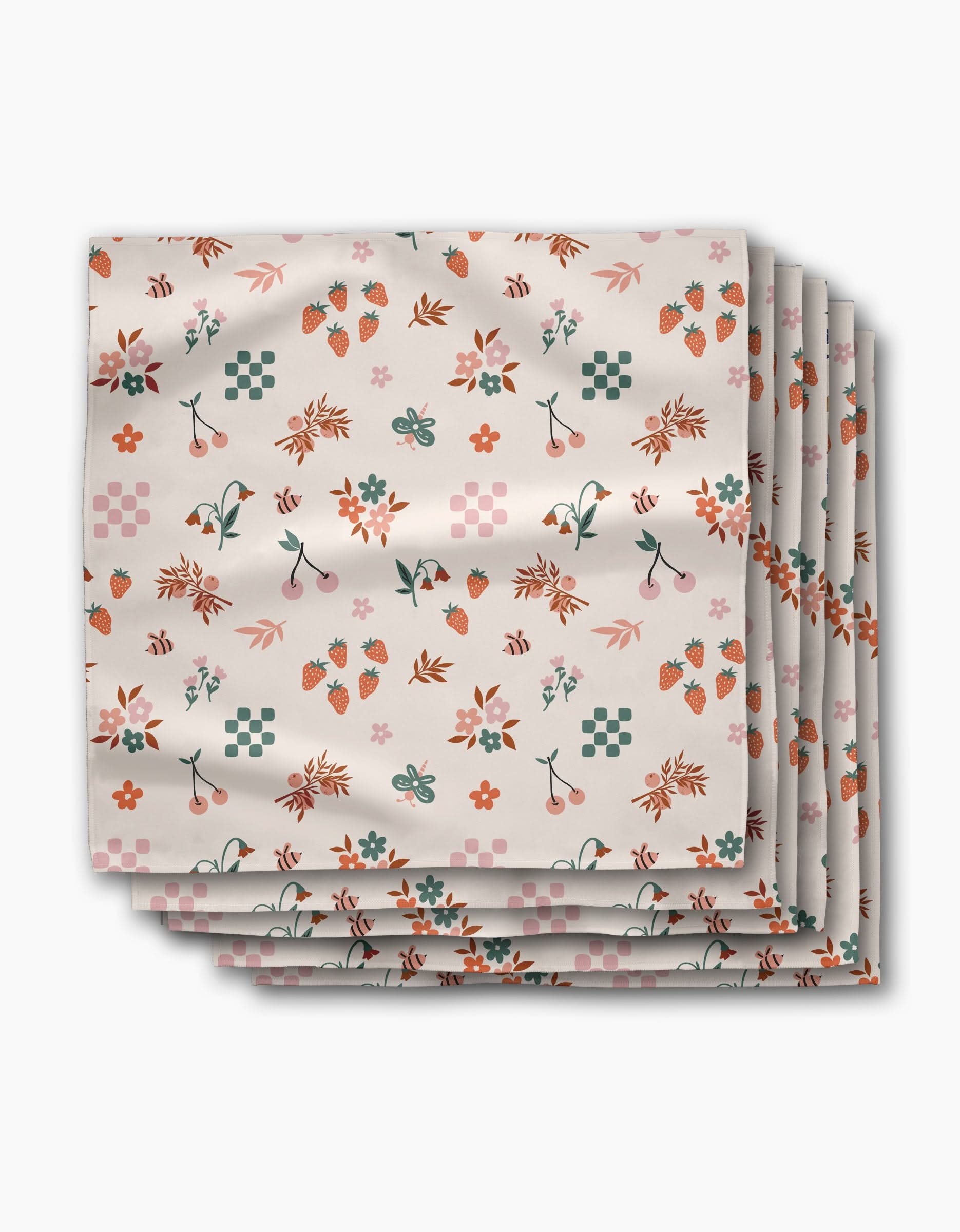 A stack of four Russet Meadow dinner napkins by Charlie Rowan Designs, made from soft Geosuede fabric, featuring a colorful pattern of flowers, leaves, strawberries, cherries, and geometric shapes on a white background.
