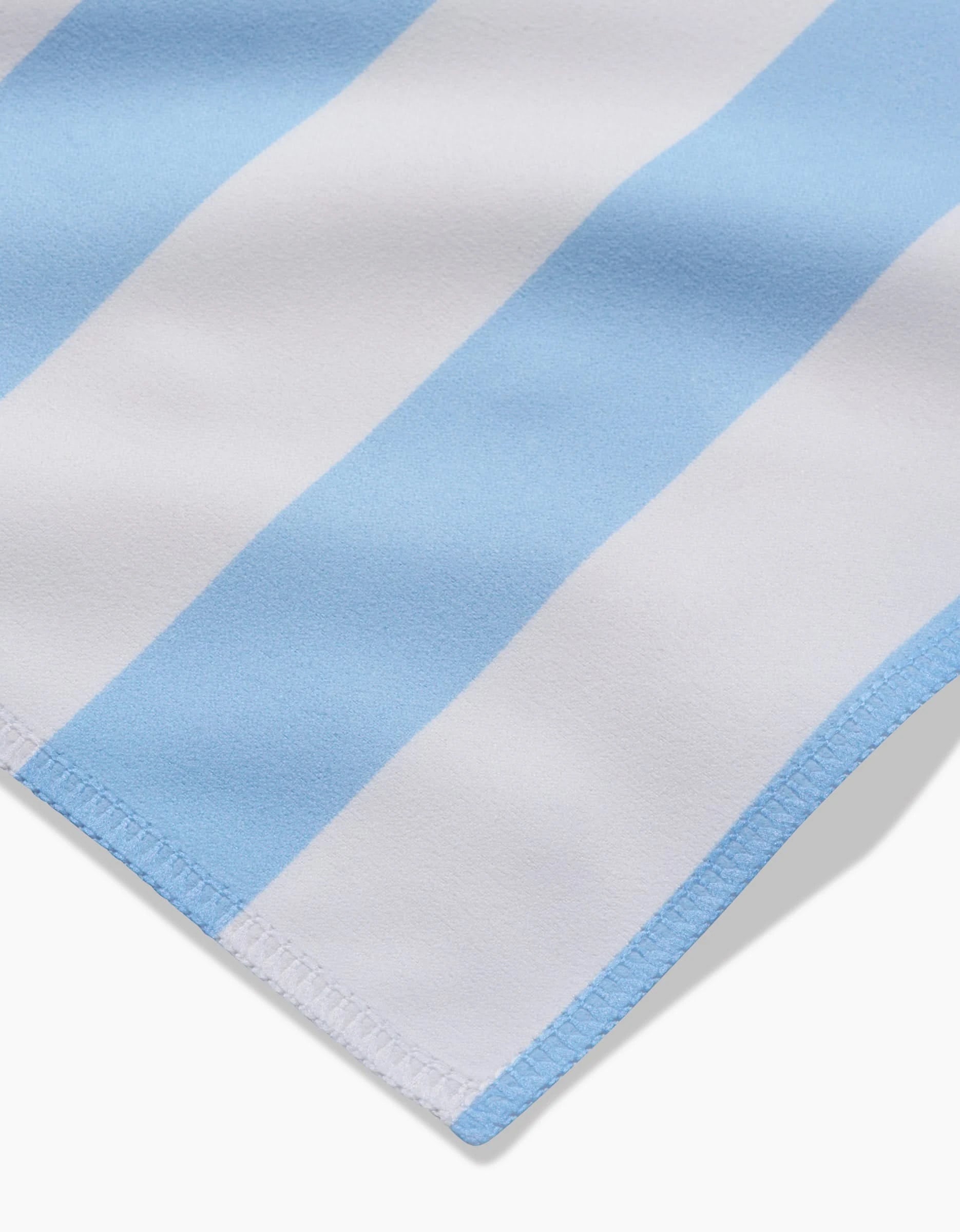 Close-up of GEOMETRYs Seaside Stripes dinner napkins, crafted from Geosuede fabric with alternating light blue and white vertical stripes and neatly stitched edges.