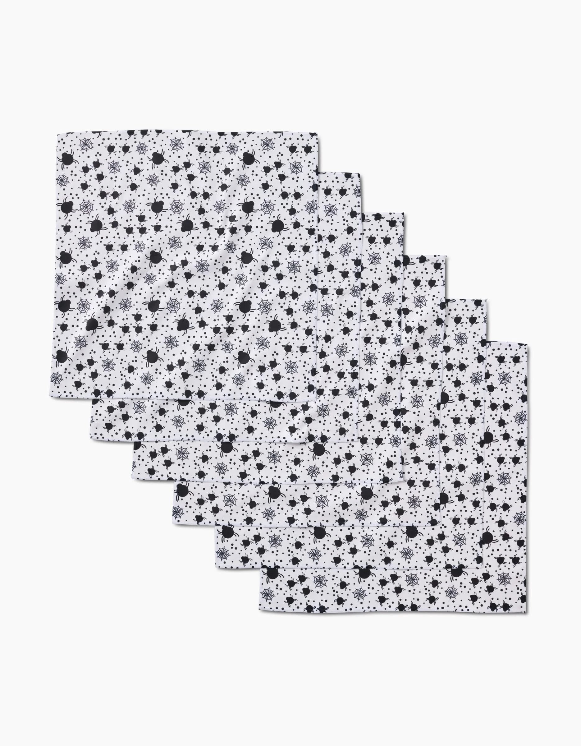 Six white Spiders For Days dinner napkins by Charlie Rowan Designs, featuring a repeating black star and dot pattern, are neatly stacked and slightly overlapping on a white background.