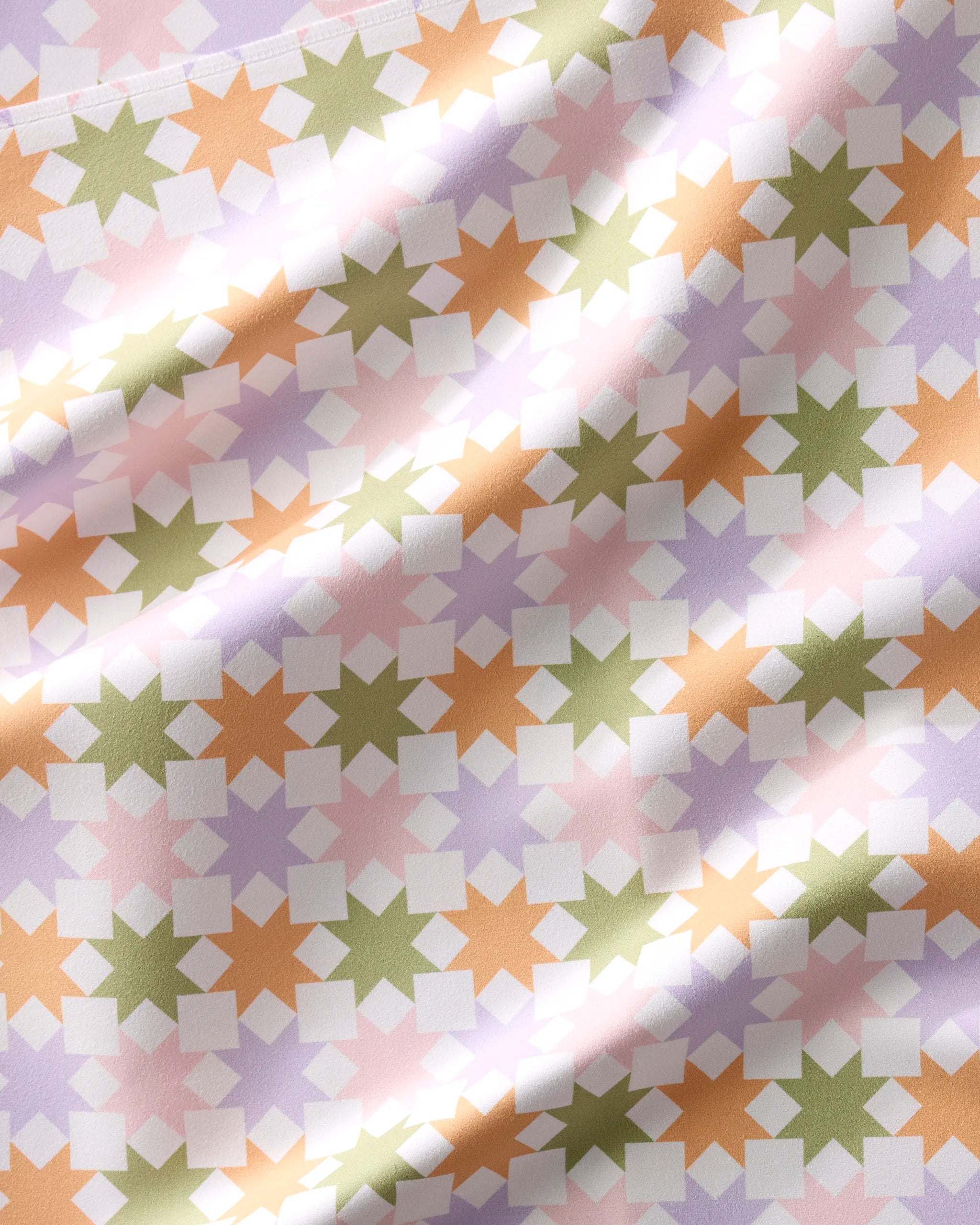 A close-up of Kayla Ann’s Spring Quilt recycled napkins shows a geometric pattern of interlocking stars and squares in pastel pink, green, peach, and lavender, with soft folds adding texture and dimension.