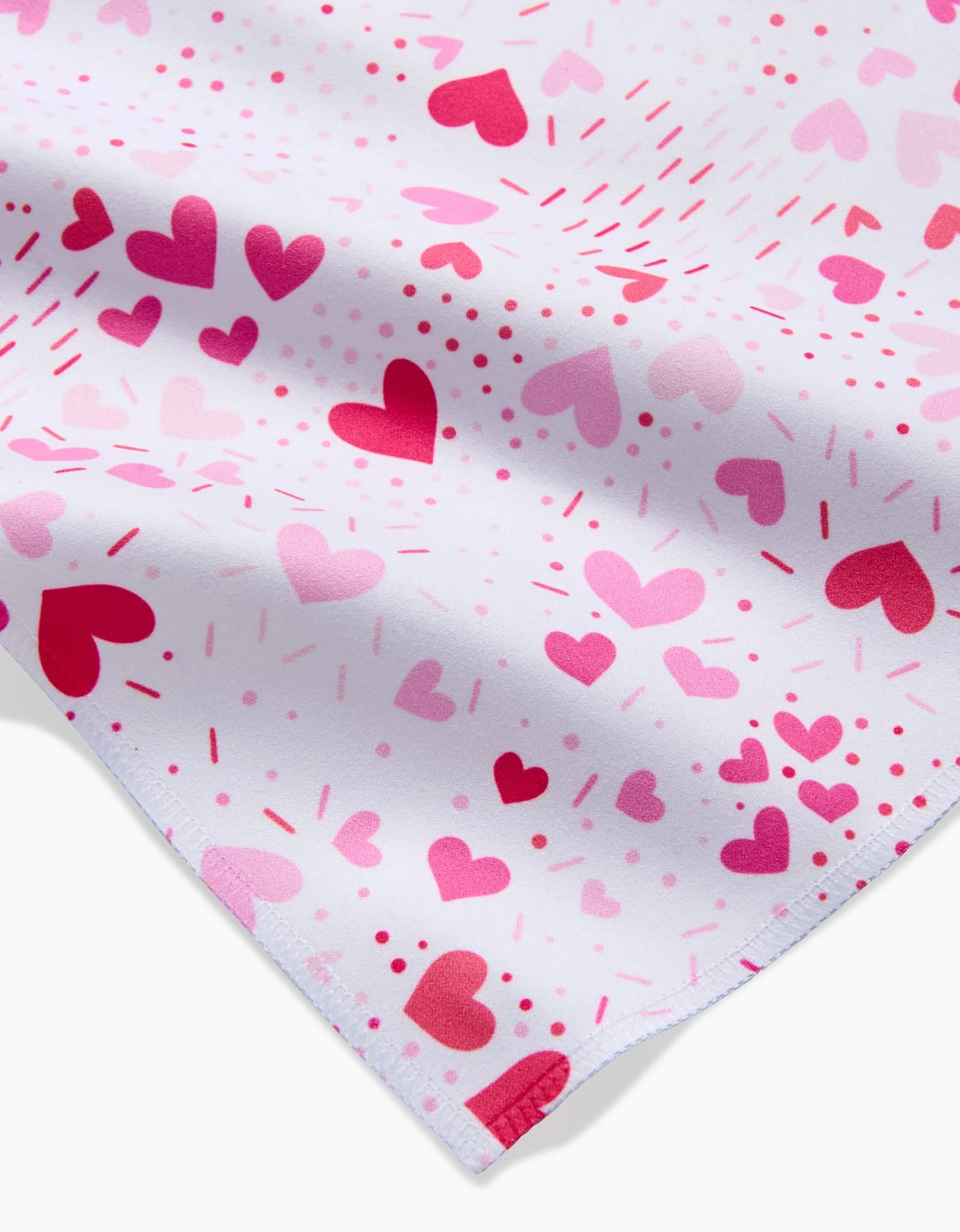 A close-up of the Sprinkled With Love napkin by Rebecca Bobko shows white fabric with pink and red hearts in various sizes and dotted accents—an eco-friendly touch to charm any dinner napkin set.