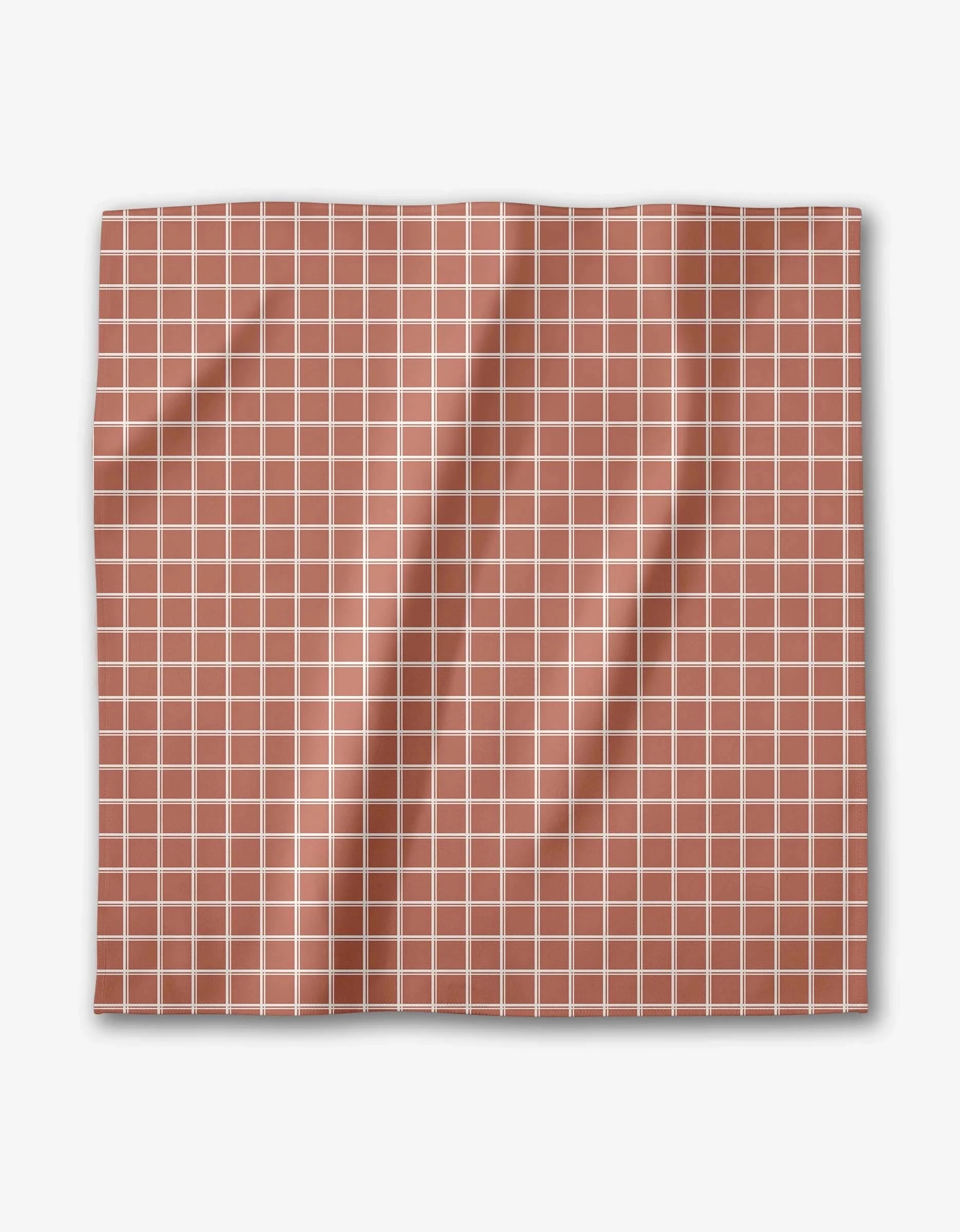 The Striped Harvest dinner napkin by Charlie Rowan Designs features a square Geosuede fabric with a terracotta background, white grid pattern, and gentle folds and creases.