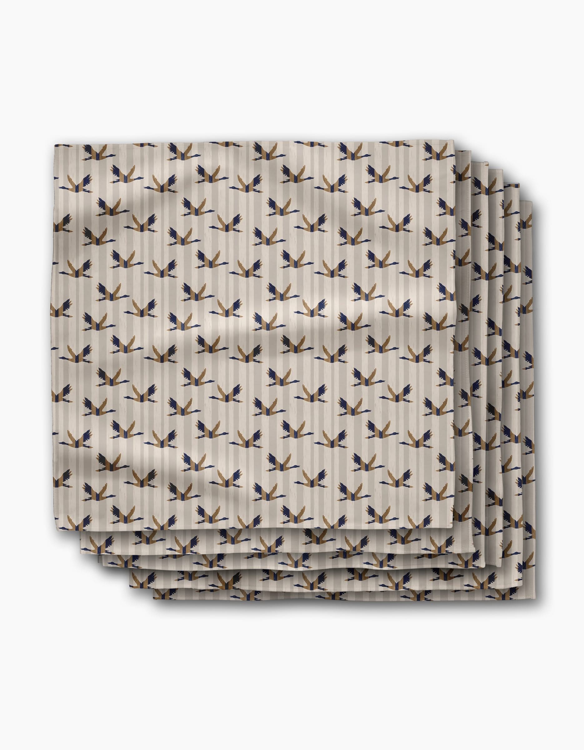 Four neatly stacked Striped Nautical Birds dinner napkins by Geometry, made from recycled Geosuede fabric. Features a white background with a repeating blue and brown bird pattern for eco-friendly, standout dining.