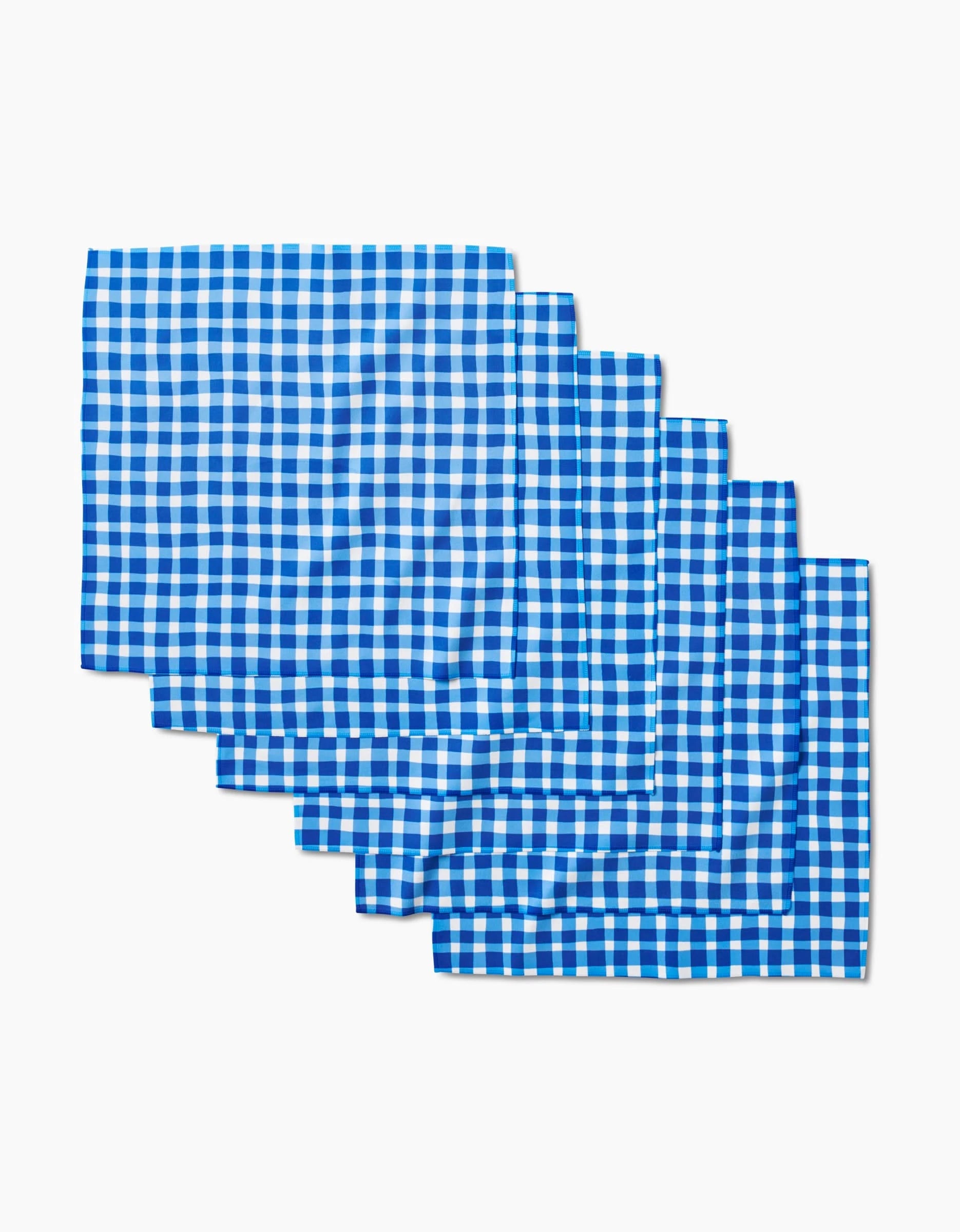 Six Summer Plaid dinner napkins by Danelys Sidron, featuring blue and white checkered Geosuede fabric, are stacked neatly on a white background.