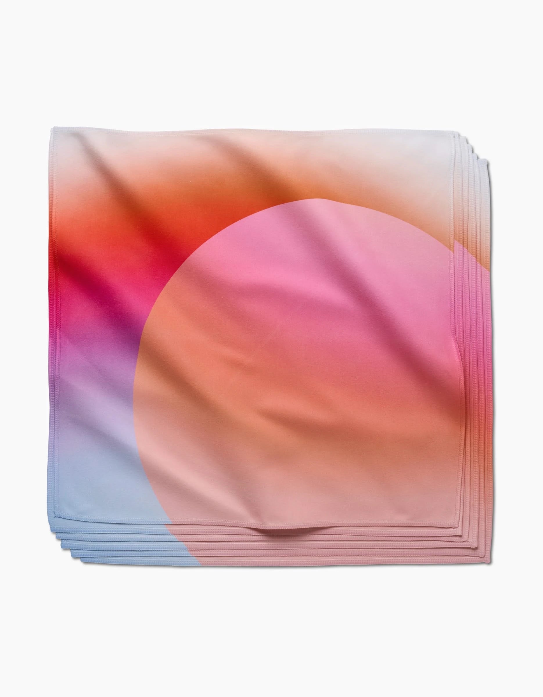 Sunrise by GEOMETRY is a folded square scarf with a gradient in pink, orange, purple, and light blue hues, crafted from recycled materials and featuring a large semi-transparent peach circle on smooth fabric.