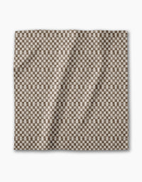 The Geometry Tavern is a square dinner napkin with a small brown and white checkerboard pattern. Eco-friendly and neatly folded, it’s showcased against a plain white background.