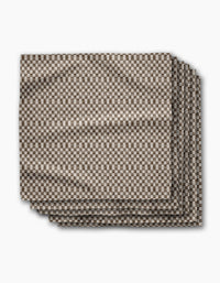 A set of four eco-friendly “Tavern” napkins by Geometry, neatly folded and displaying a small brown and white checkerboard pattern against a white background.