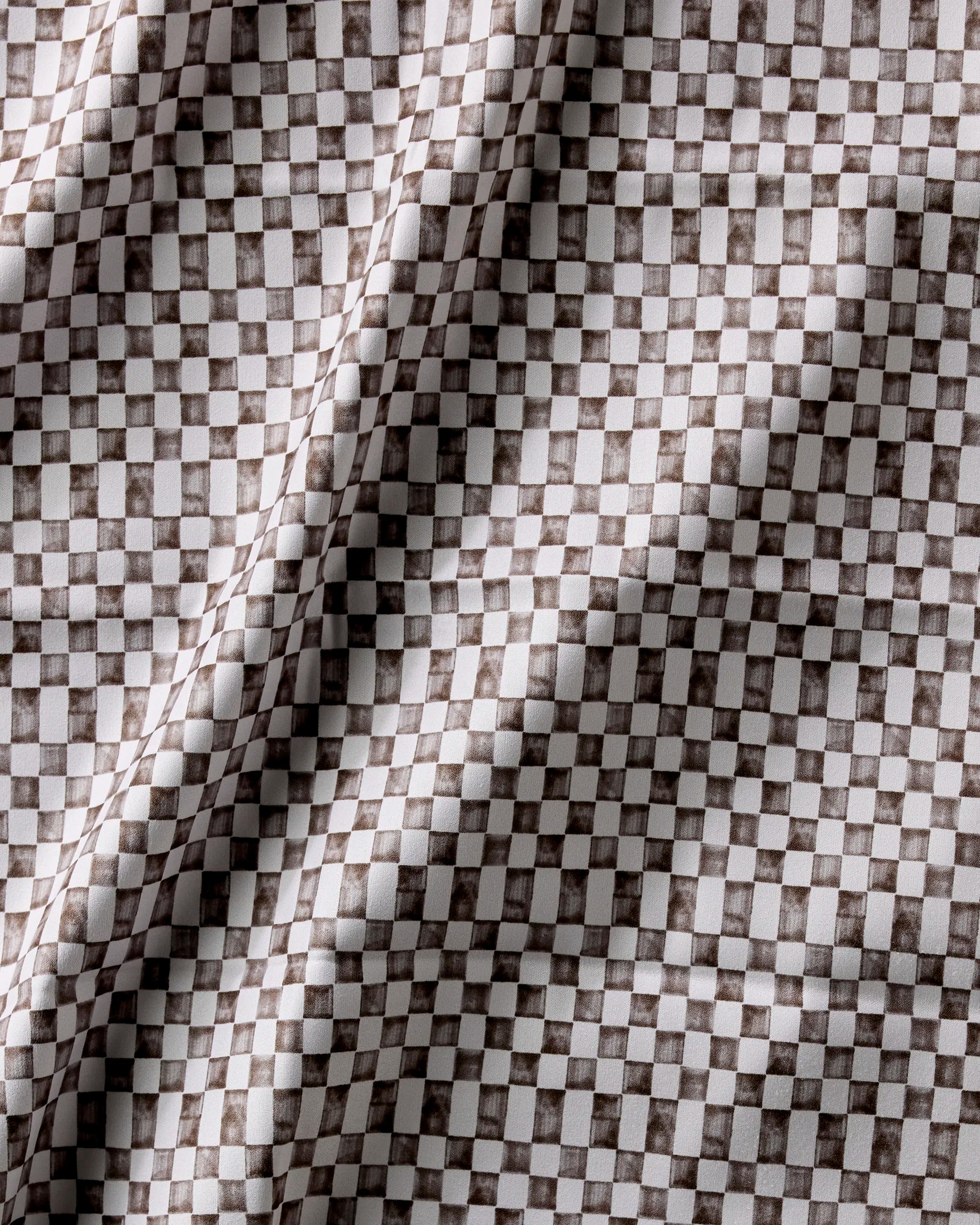 A close-up of Geometry's Tavern washable cloth napkins features a brown and white checkerboard pattern, with gentle folds and shadows highlighting the textured surface.