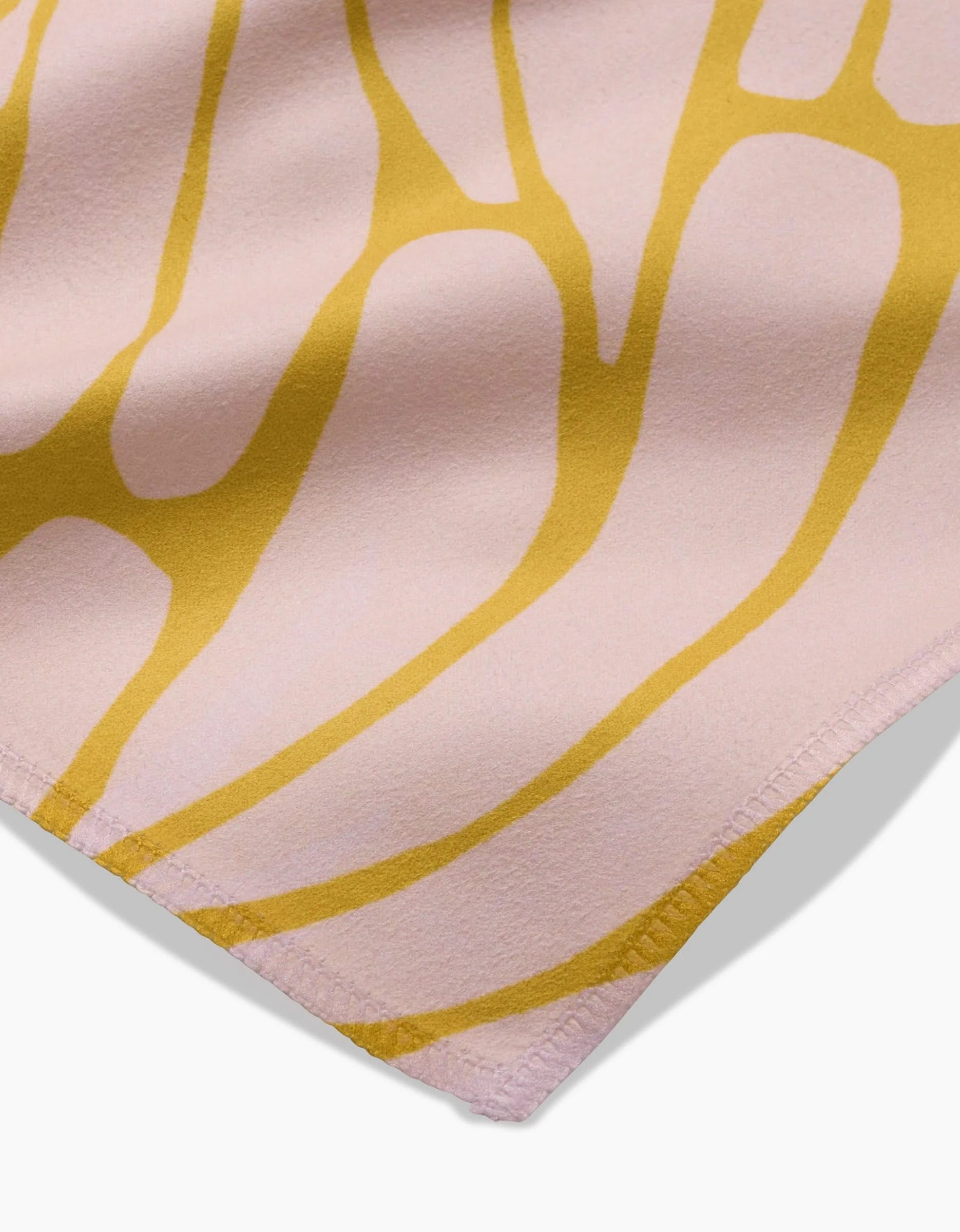 A close-up of the GEOMETRY Tenderhearted dinner napkin in light pink Geosuede fabric, featuring neatly hemmed corners and abstract yellow, nature-inspired lines for a minimalist look.