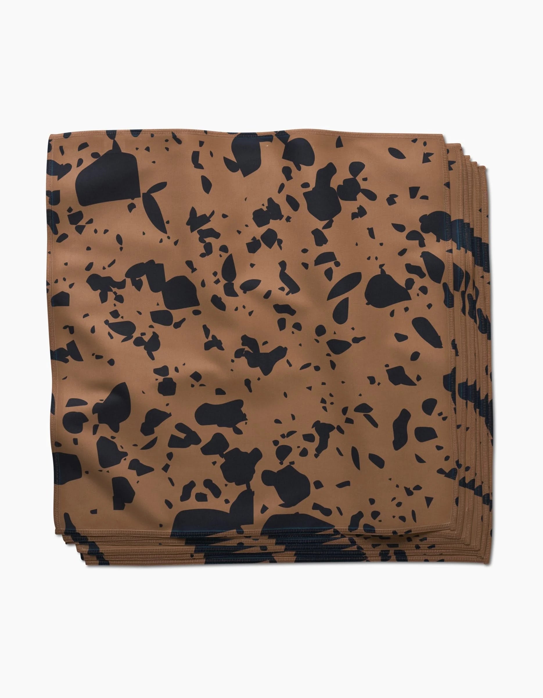 The GEOMETRY Terrazo dinner napkin is a neatly folded brown recycled napkin with an irregular black speckled pattern, showcased against a plain white background.