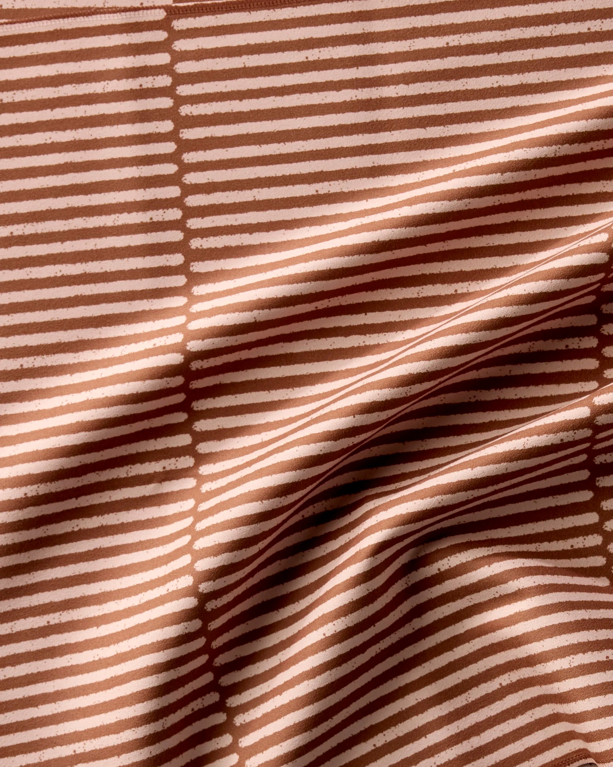 A close-up of Rosa Kichline’s Textured Stripe reusable napkin shows light pink fabric with evenly spaced horizontal white lines and soft folds, highlighting its textured surface.
