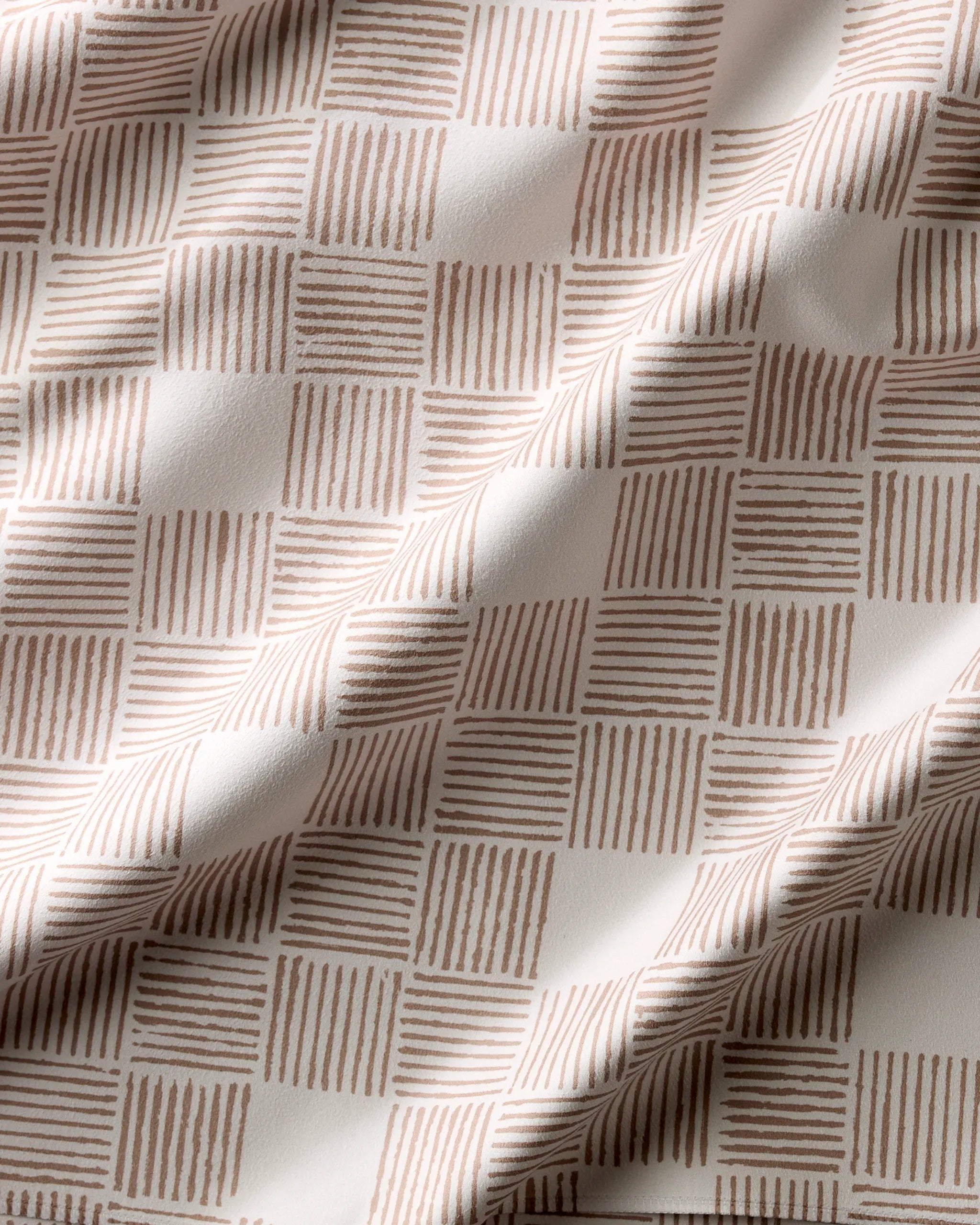 Thatcher by Studio Jeannot features Geosuede fabric in a grid of alternating beige squares and beige squares with vertical lines on white. Its soft drape and gentle folds make it ideal for recycled dinner napkins.
