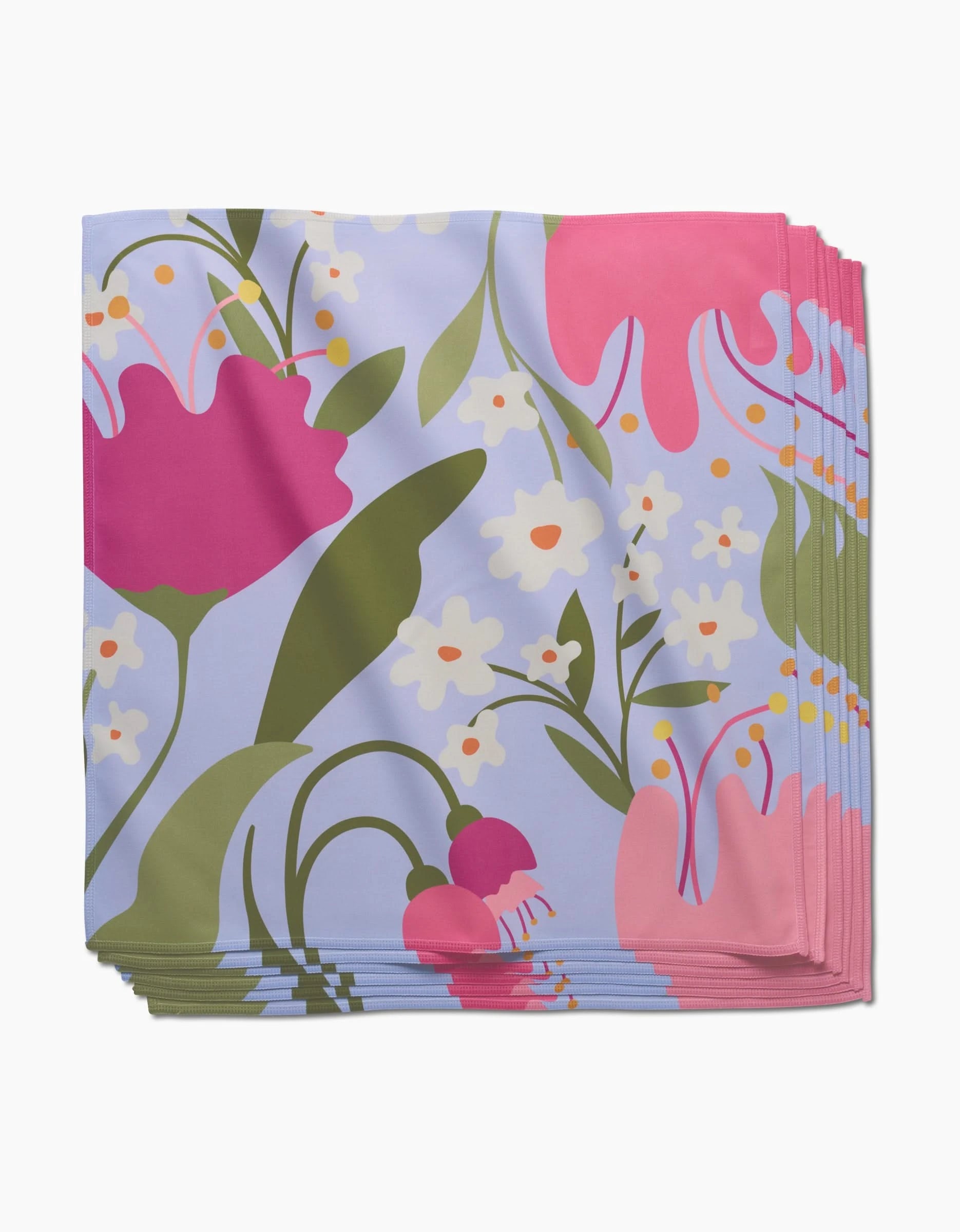 A stack of GEOMETRY Thoughtful dinner napkins made from soft, recycled Geosuede fabric, featuring a colorful floral pattern with pink, white, and purple flowers plus green leaves on a light purple background.