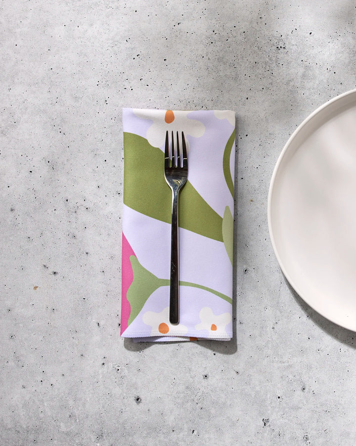 A fork rests on GEOMETRY’s Thoughtful colorful recycled dinner napkin beside a plain white plate on a light, speckled concrete surface, with dappled sunlight casting soft shadows across the table.