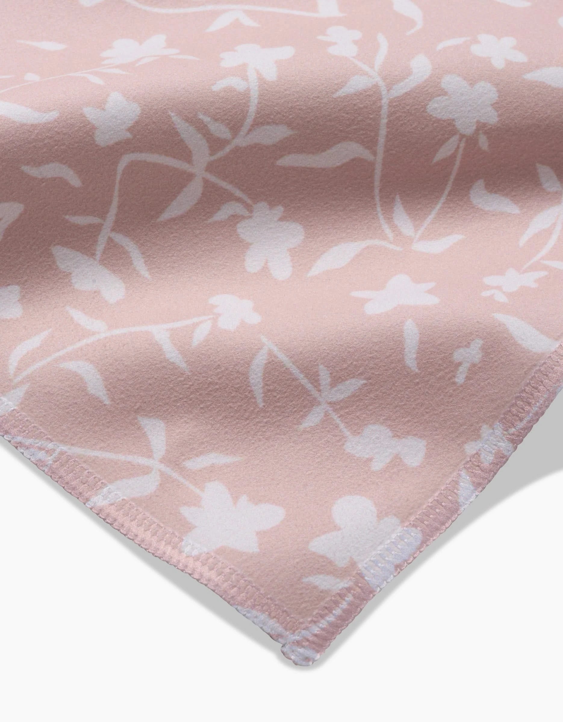 A close-up of Aubrey Fairchild’s Tiny Floral shows soft pink Geosuede fabric with white floral patterns and stitched edges—ideal for creating elegant dinner napkins.