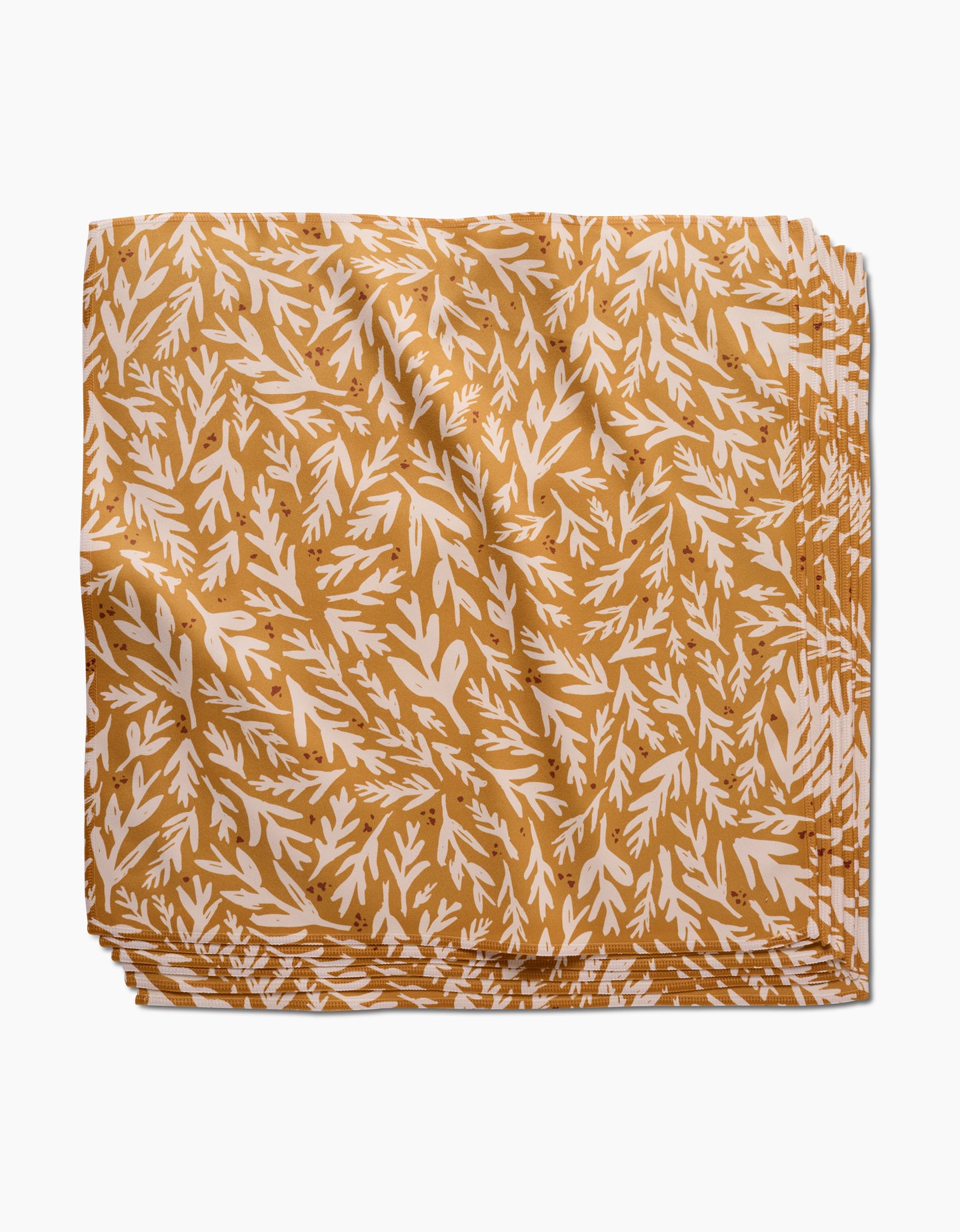 The Trail Dusting Gold napkin by Twig + Spark features an absorbent, golden yellow cloth with a white leafy branch pattern, neatly folded and stacked on a plain white surface.