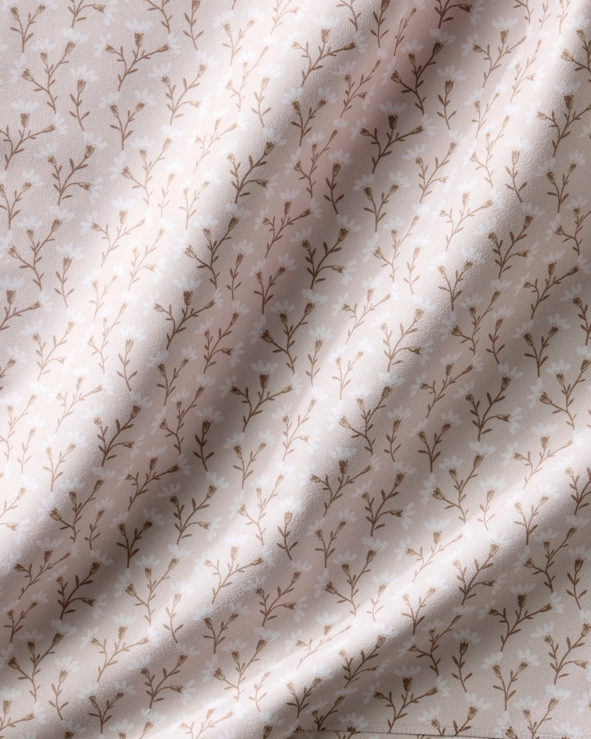 A close-up of Teri the Butter’s Trailing Flowers in Pink napkins, featuring soft, light pink recycled fabric with a delicate brown vine and leaf pattern and gentle highlights on their eco-friendly surface.