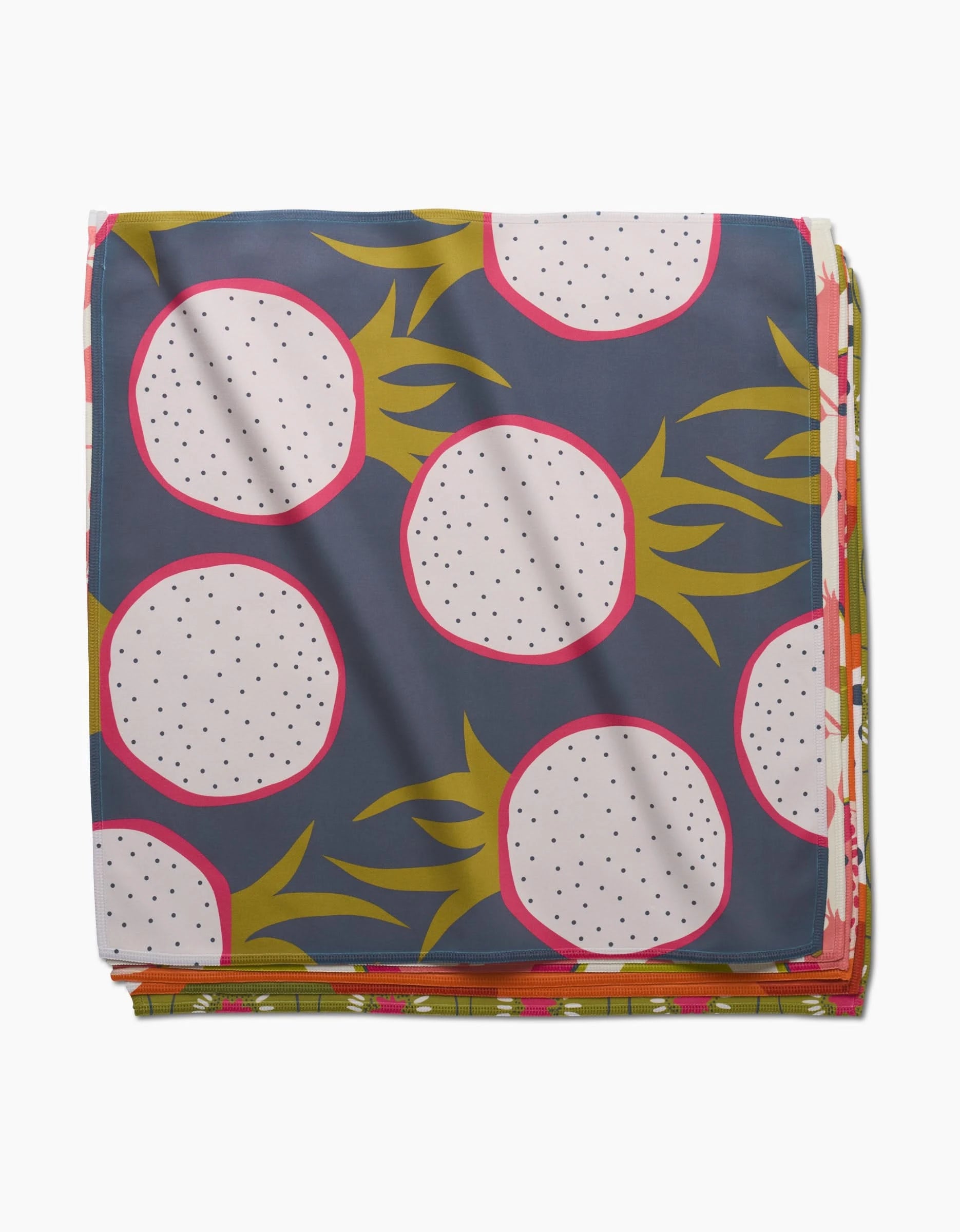 The Tropical Fruit Dinner Napkin Set by Lizzie Clark features a bold dragon fruit print—white fruit, pink borders, yellow-green leaves on dark blue—crafted from soft Geosuede fabric.