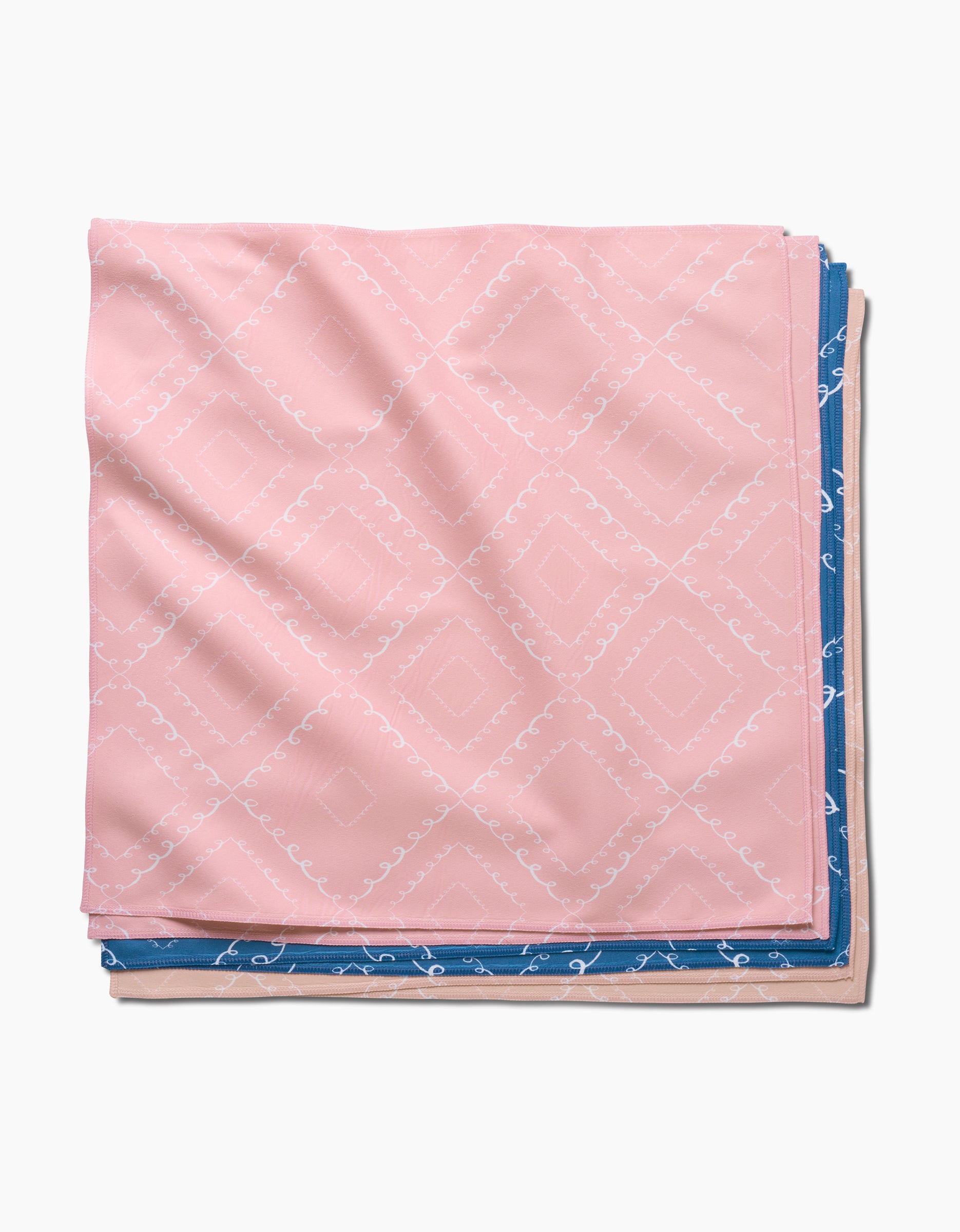 The Twirls handkerchief by Elena Fay, featuring a pink base with a white geometric pattern, is neatly folded and overlaps a blue napkin with a white design, both arranged on a plain white background.