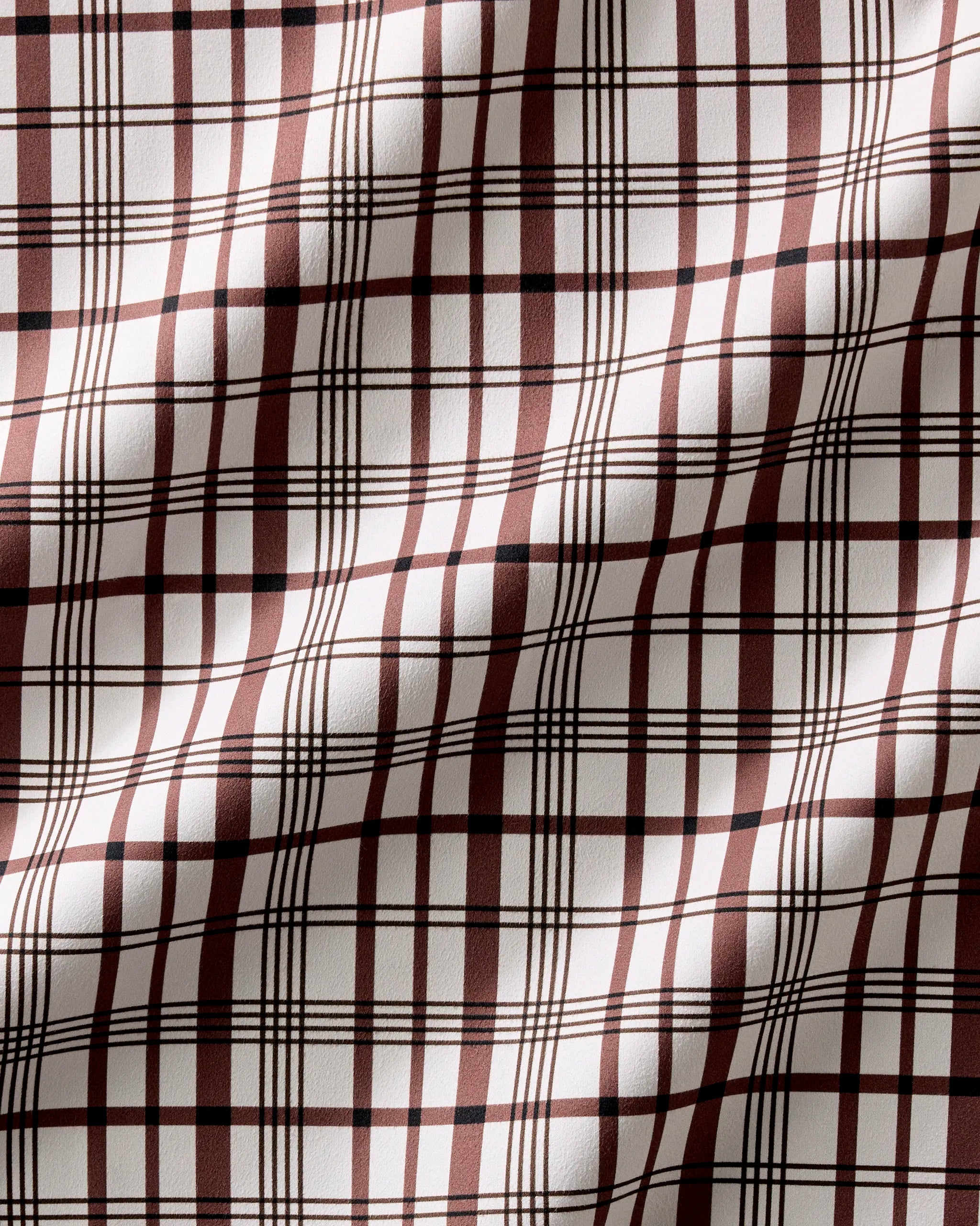 A close-up of Hufton Studio's Vintage Plaid Natural shows its brown and white intersecting lines. The textured, slightly wrinkled fabric is perfect for recycled dinner napkins, highlighted beautifully by the lighting.