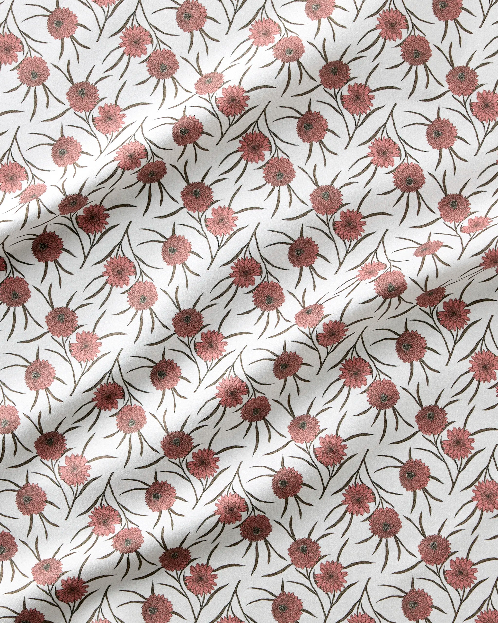 The Geometry Wild Dahlia dinner napkin set features a white fabric with a repeating wild dahlia flower pattern in pinkish-red and greenish-brown hues. Soft folds create gentle shadows across these absorbent, stylish cloth napkins.