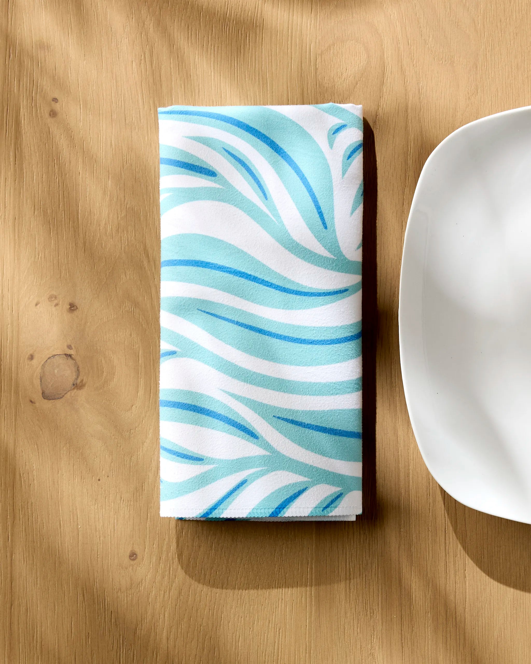 The Willow Wave reusable table napkin by Rachel Parker rests on the table, ready to bring an eco-friendly touch to your dining experience.