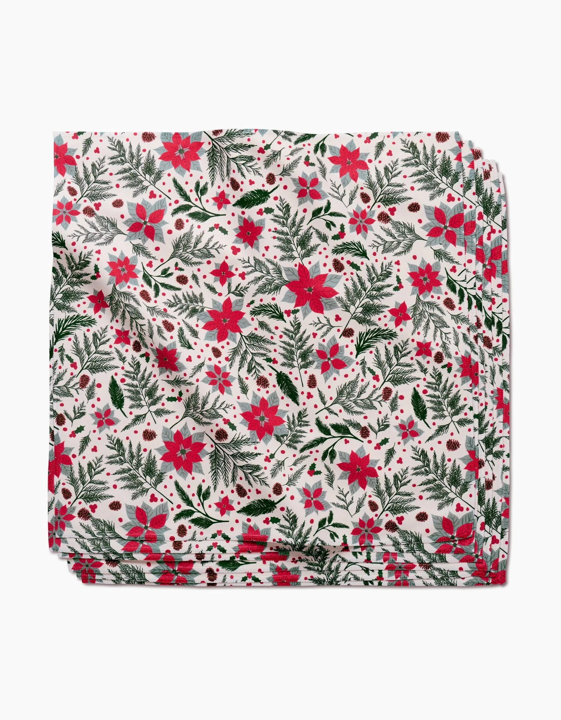 A folded dinner napkin from the Rebecca Bobko Woodland Poinsettia set, featuring red poinsettias, green pine branches, and small red berries on white Geosuede fabric.