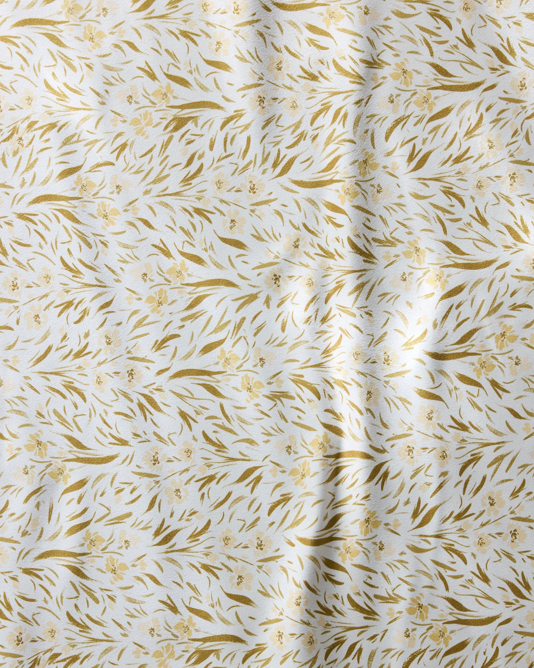 Melissa Johnson's Yellow Floral napkin set features white recycled fabric with a subtle sheen and a gold leafy floral pattern. Gentle folds create soft shadows, adding texture and elegance to these reusable dinner napkins.