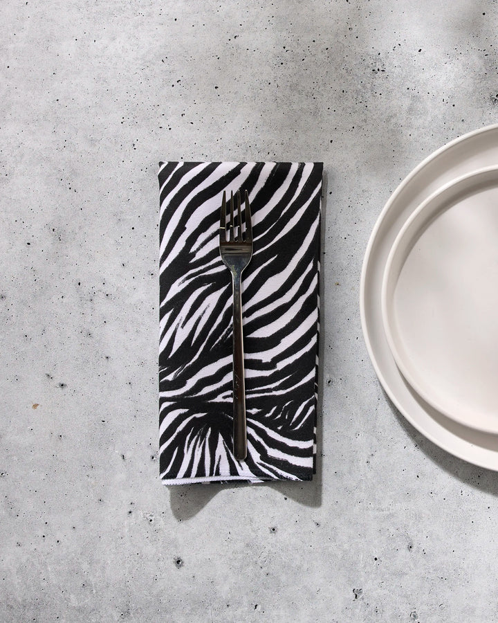 A fork rests on the GEOMETRY Zebra reusable cloth napkin beside a white plate atop a gray, speckled surface.