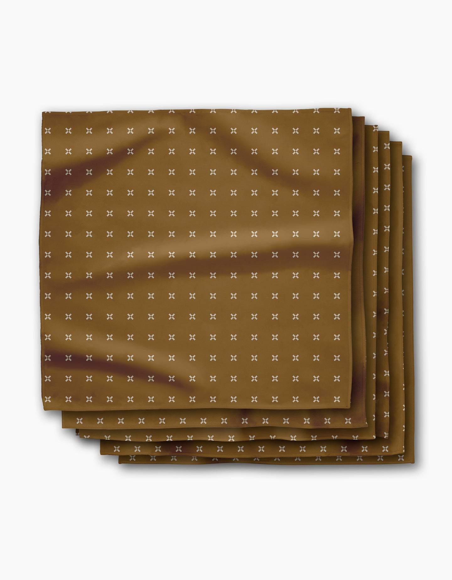 The Amber Stitch napkin by Geometry features brown Geosuede fabric with a subtle white X pattern, neatly folded into four layers and displayed on a white background.