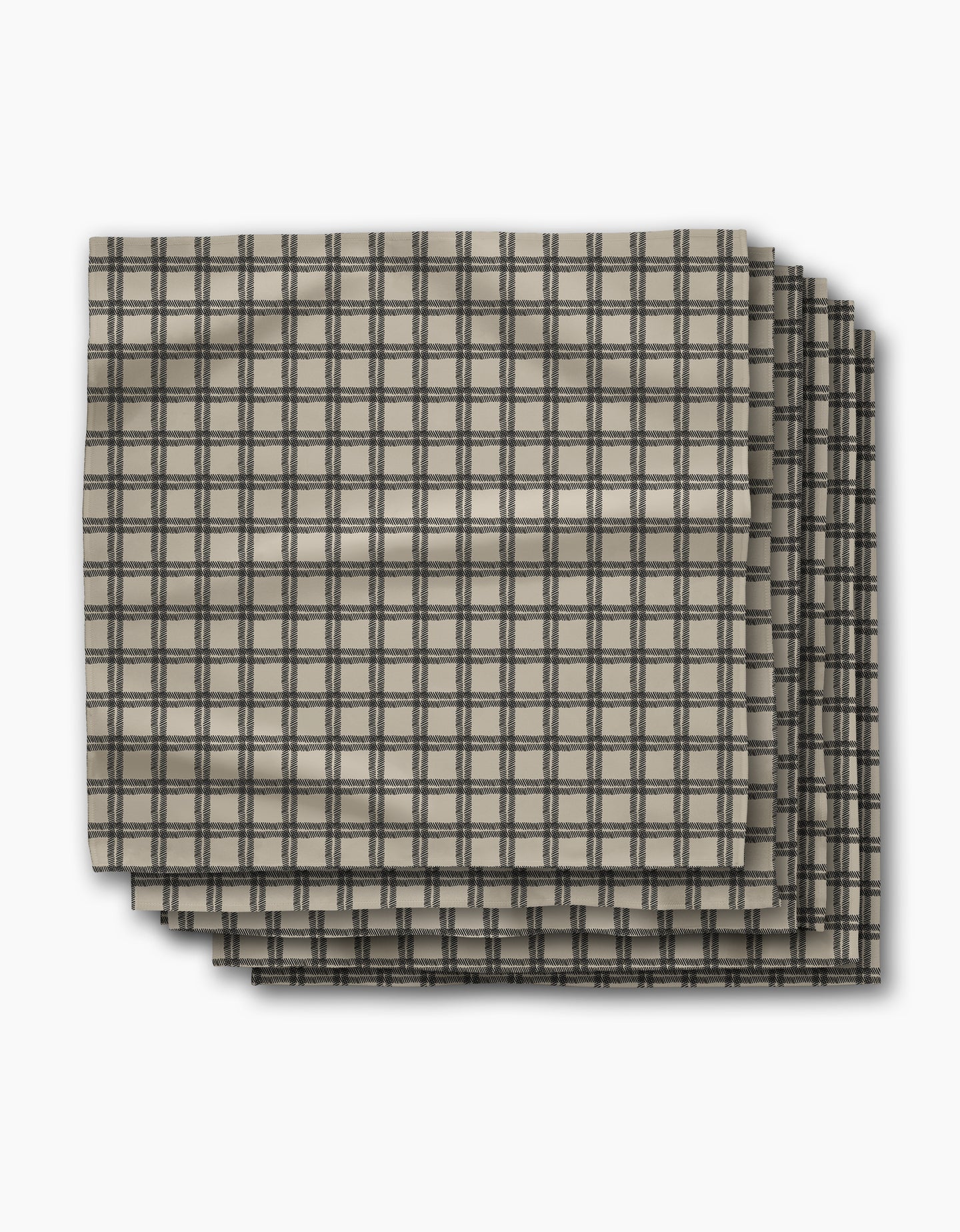 Four beige fabric napkins with a black grid plaid pattern, the Blackstone Dinner Napkin Set by Geometry, are neatly stacked. Crafted from absorbent recycled materials, this set is both stylish and practical.
