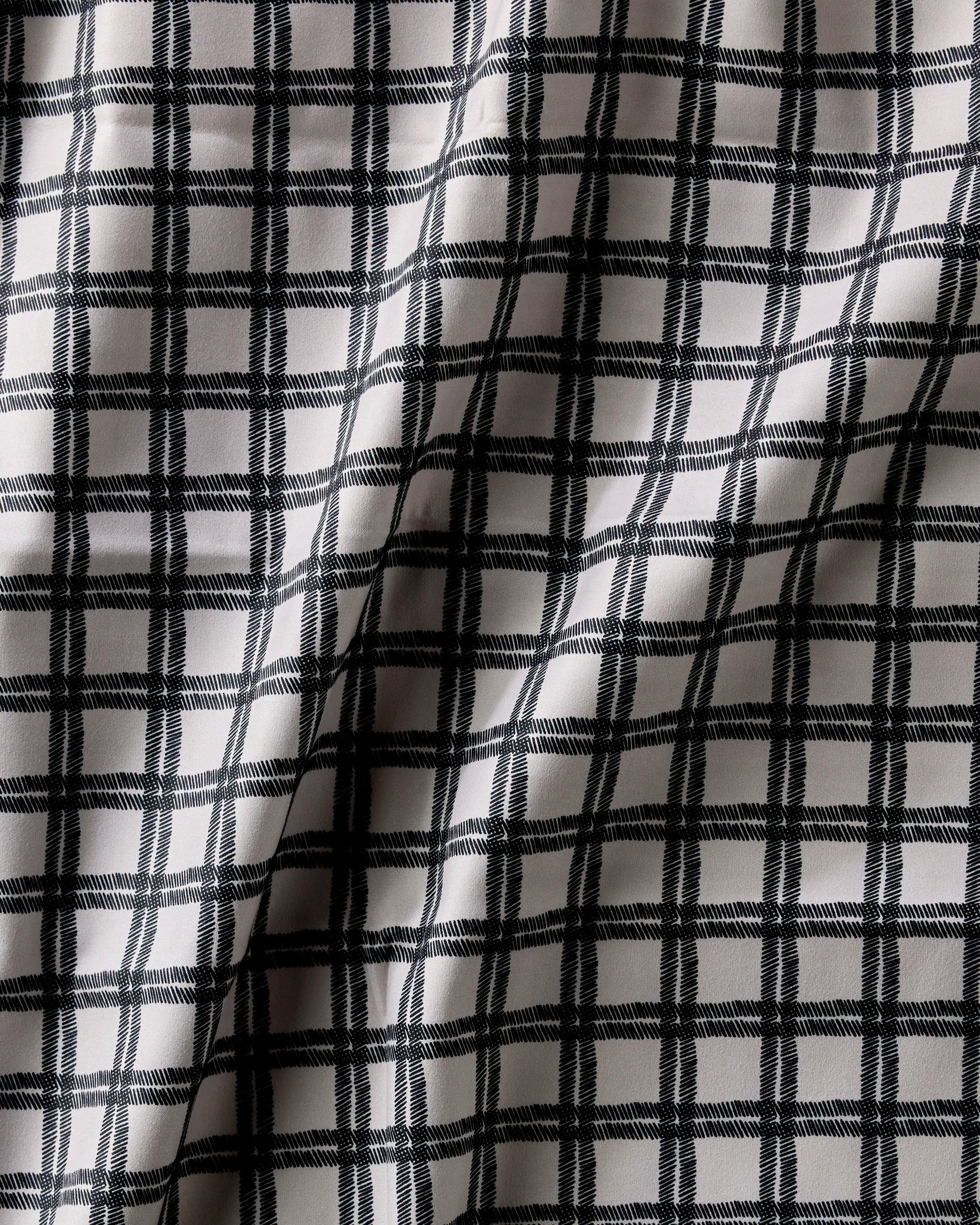 A close-up of Geometry's Blackstone fabric, showcasing its black and white checkered grid pattern with soft folds—ideal for eco-friendly table linens or a chic Dinner Napkin Set.