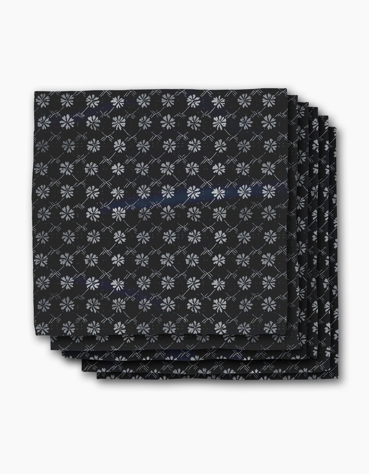 Four neatly stacked Bonnie Indigo napkins by Geometry, featuring a repeating white snowflake-like pattern on black, displayed against a plain white background.