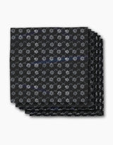Four neatly stacked Bonnie Indigo napkins by Geometry, featuring a repeating white snowflake-like pattern on black, displayed against a plain white background.