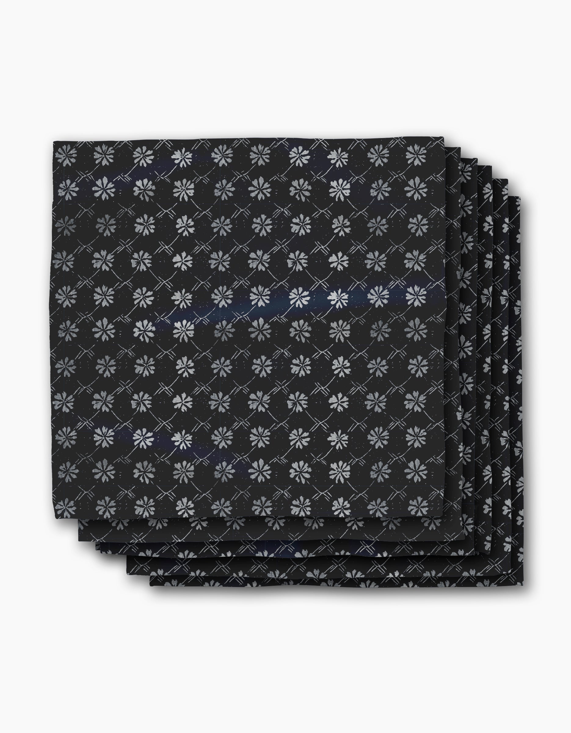 Four neatly stacked Bonnie Indigo napkins by Geometry, featuring a repeating white snowflake-like pattern on black, displayed against a plain white background.