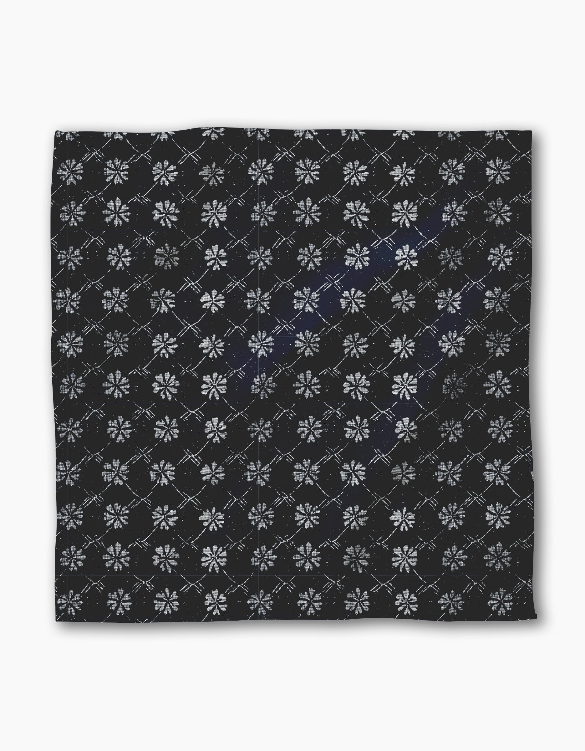 The Geometry Bonnie Indigo is a square black recycled dinner napkin featuring light gray geometric floral patterns and intersecting diamond lines, combining style and absorbency for any dinner setting.