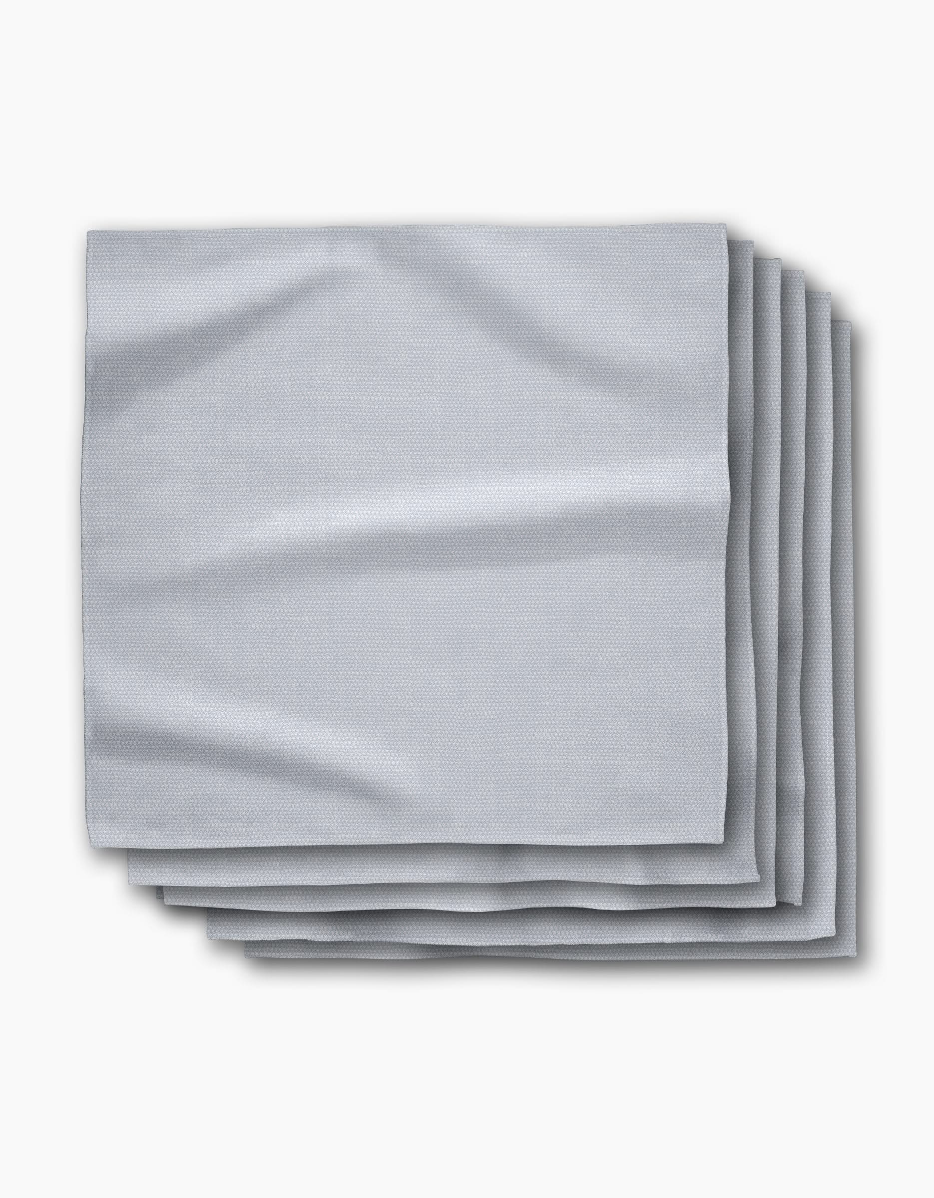 A stack of five Chambray Light Blue absorbent cloth napkins by Geometry is neatly folded on a white background, showcasing their smooth texture and subtle creases.
