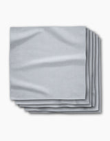 A stack of five Chambray Light Blue absorbent cloth napkins by Geometry is neatly folded on a white background, showcasing their smooth texture and subtle creases.