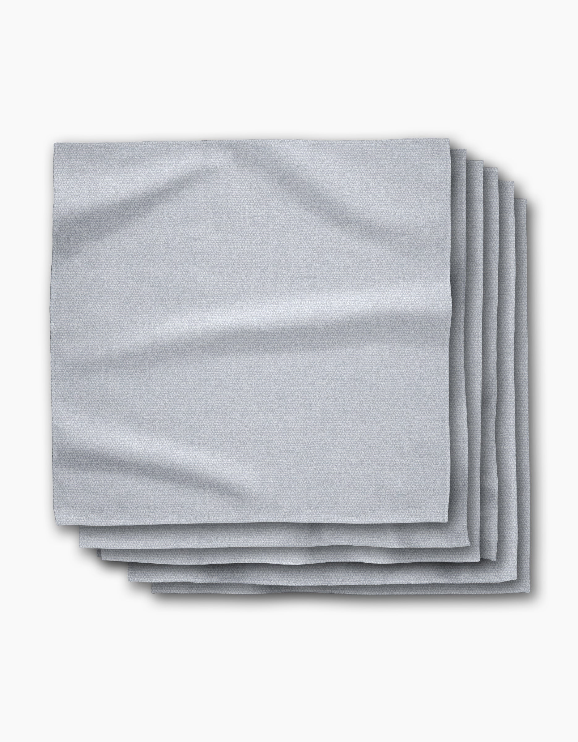 A stack of five Chambray Light Blue absorbent cloth napkins by Geometry is neatly folded on a white background, showcasing their smooth texture and subtle creases.
