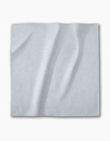 A Chambray Light Blue napkin from Geometry—a square, light gray-blue recycled fabric with a subtle textured pattern—lies flat on a white background. The absorbent cloth is part of an eco-friendly dinner napkin set.