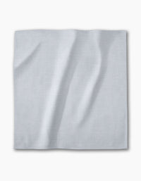 A Chambray Light Blue napkin from Geometry—a square, light gray-blue recycled fabric with a subtle textured pattern—lies flat on a white background. The absorbent cloth is part of an eco-friendly dinner napkin set.